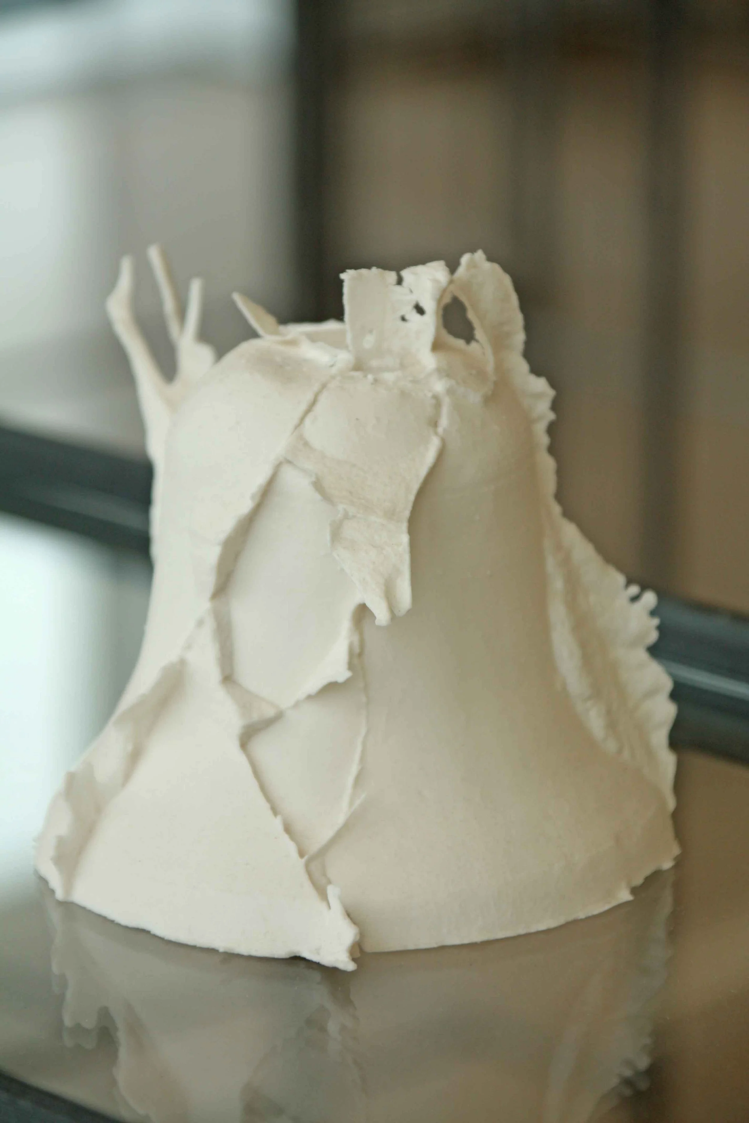 Close-up of a ceramic bell and decorative white curls on top, reflecting on a metallic surface.