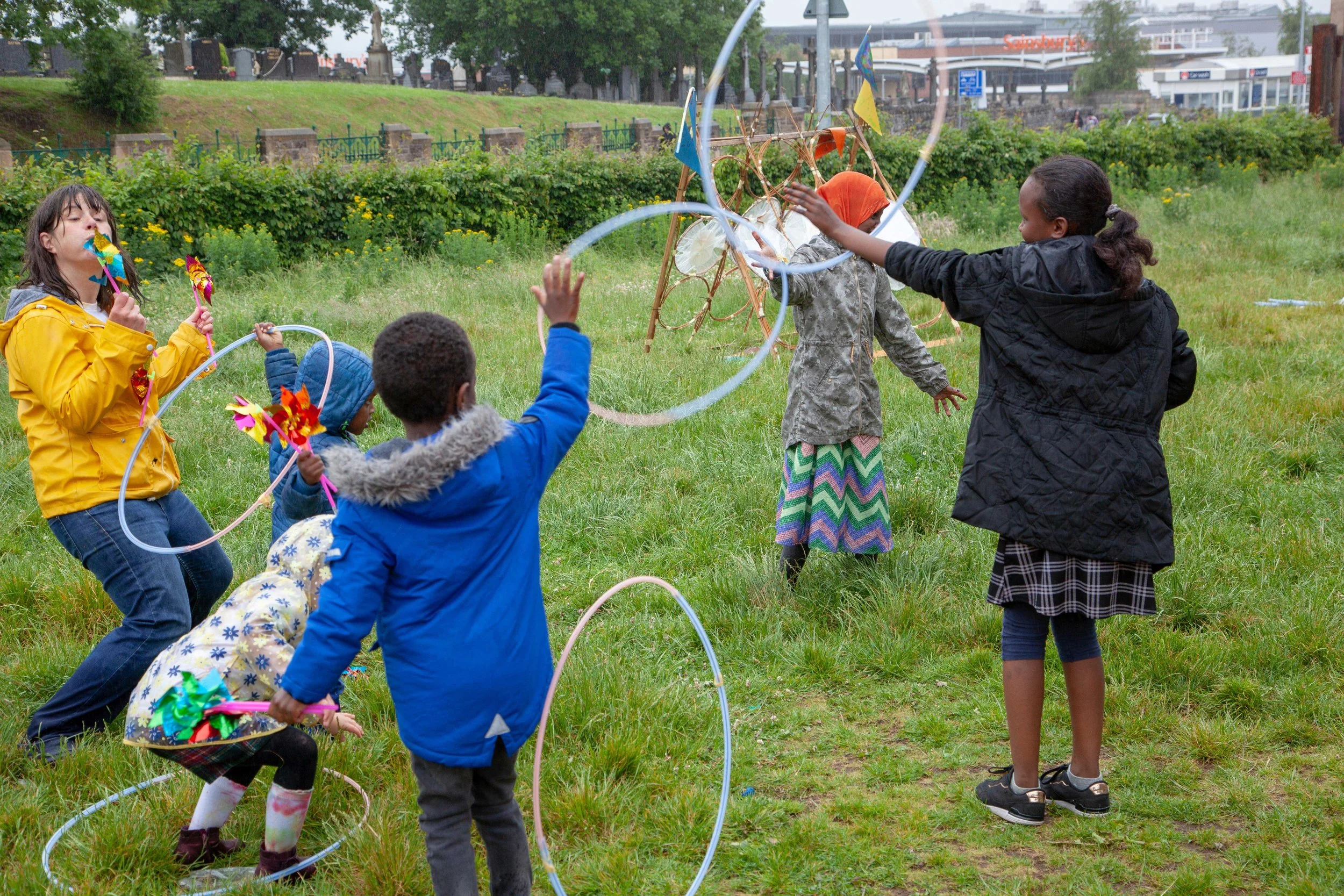Children playing with hula hoops and pinwheels in a grassy outdoor area during the daytime.