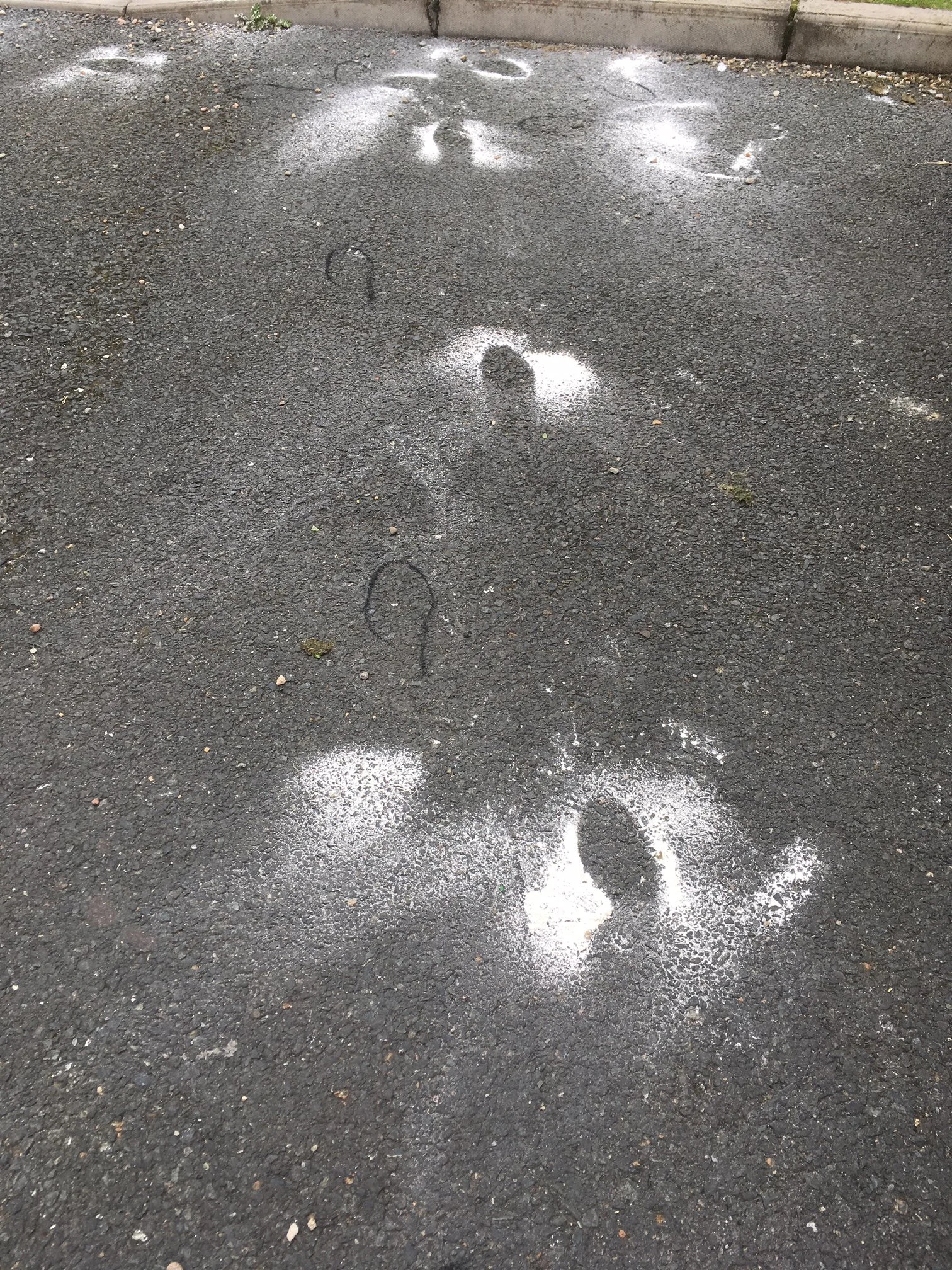 Footprints and chalk markings on asphalt ground, possibly from a game or activity.