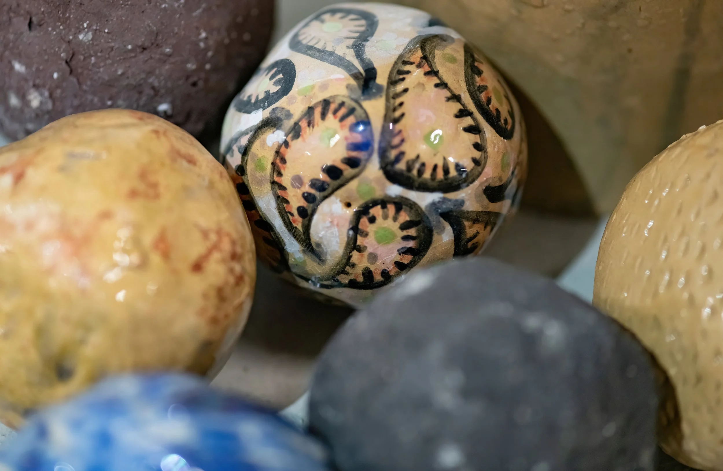 Painted ball with black, green, and pink swirl and dot designs surrounded by unpainted balls.