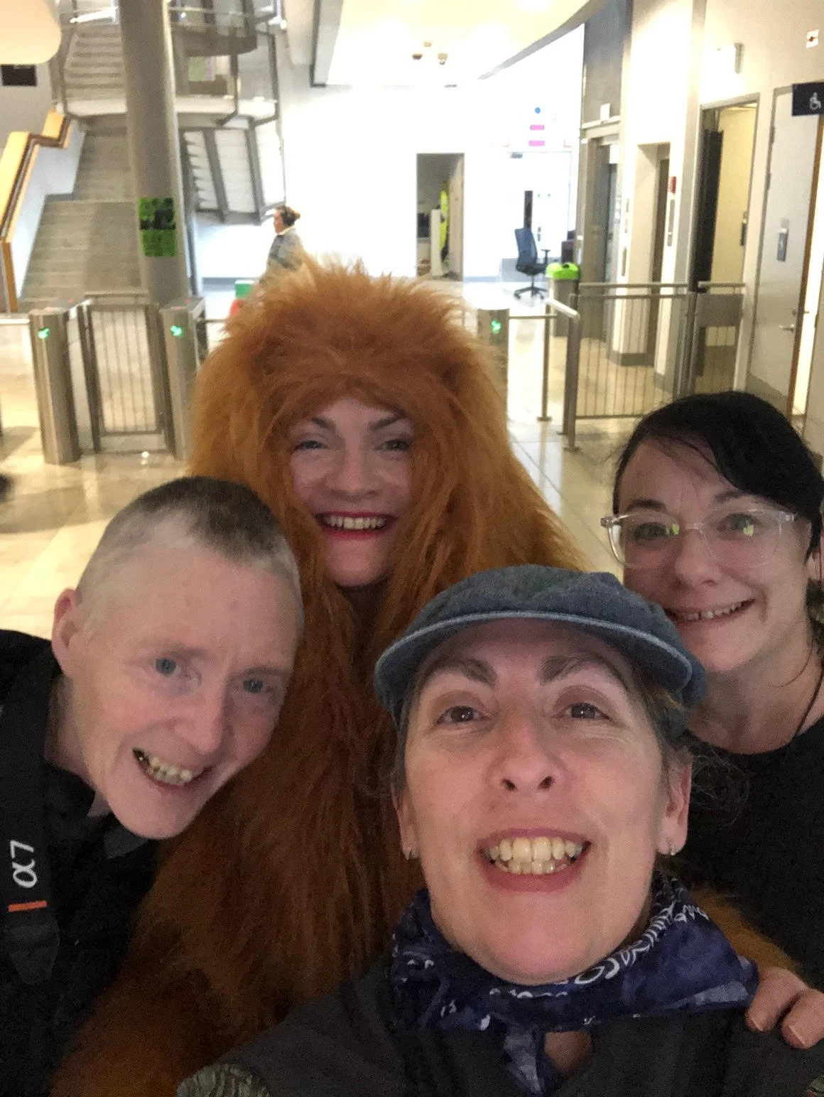 Four people taking a selfie with a person dressed in a lion costume in an indoor public space, Ulster University.