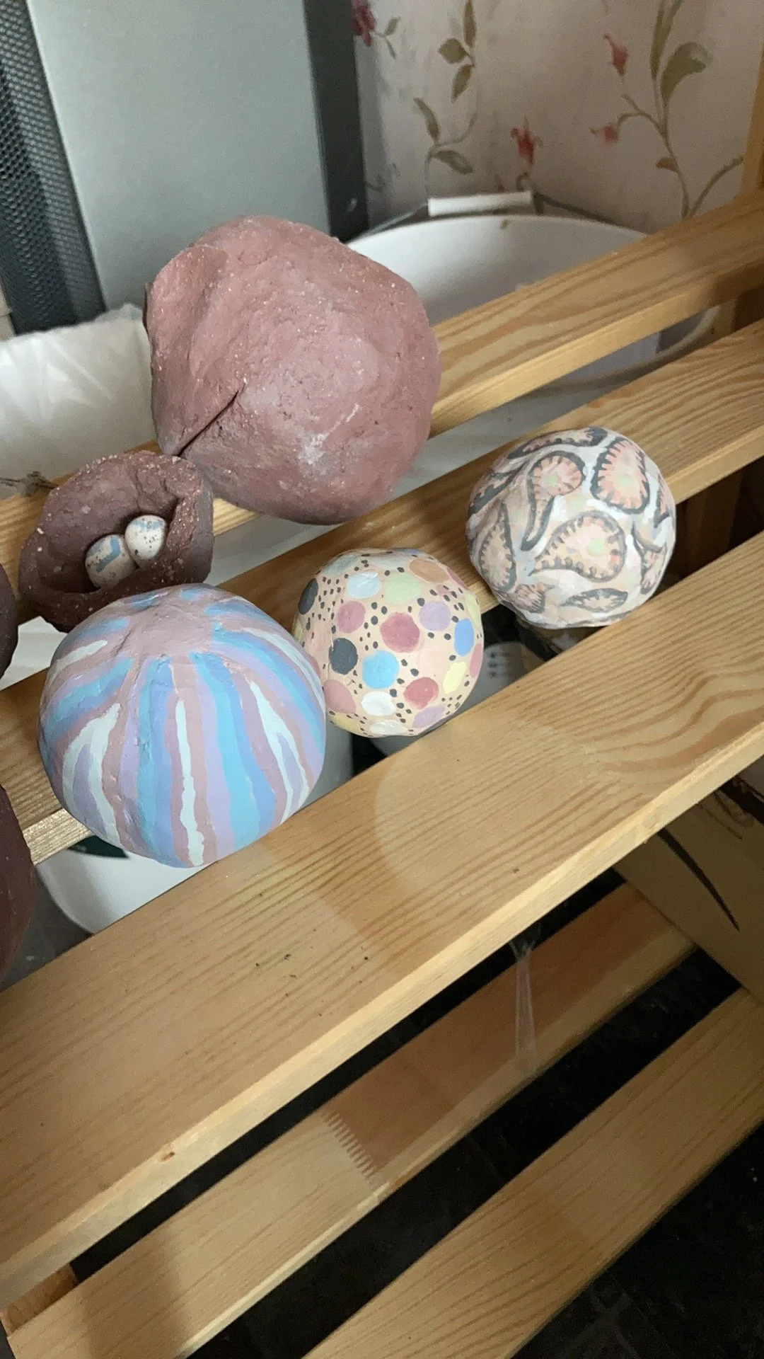 Handmade clay or ceramic decorative balls with colorful painted patterns resting on a wooden slatted shelf.