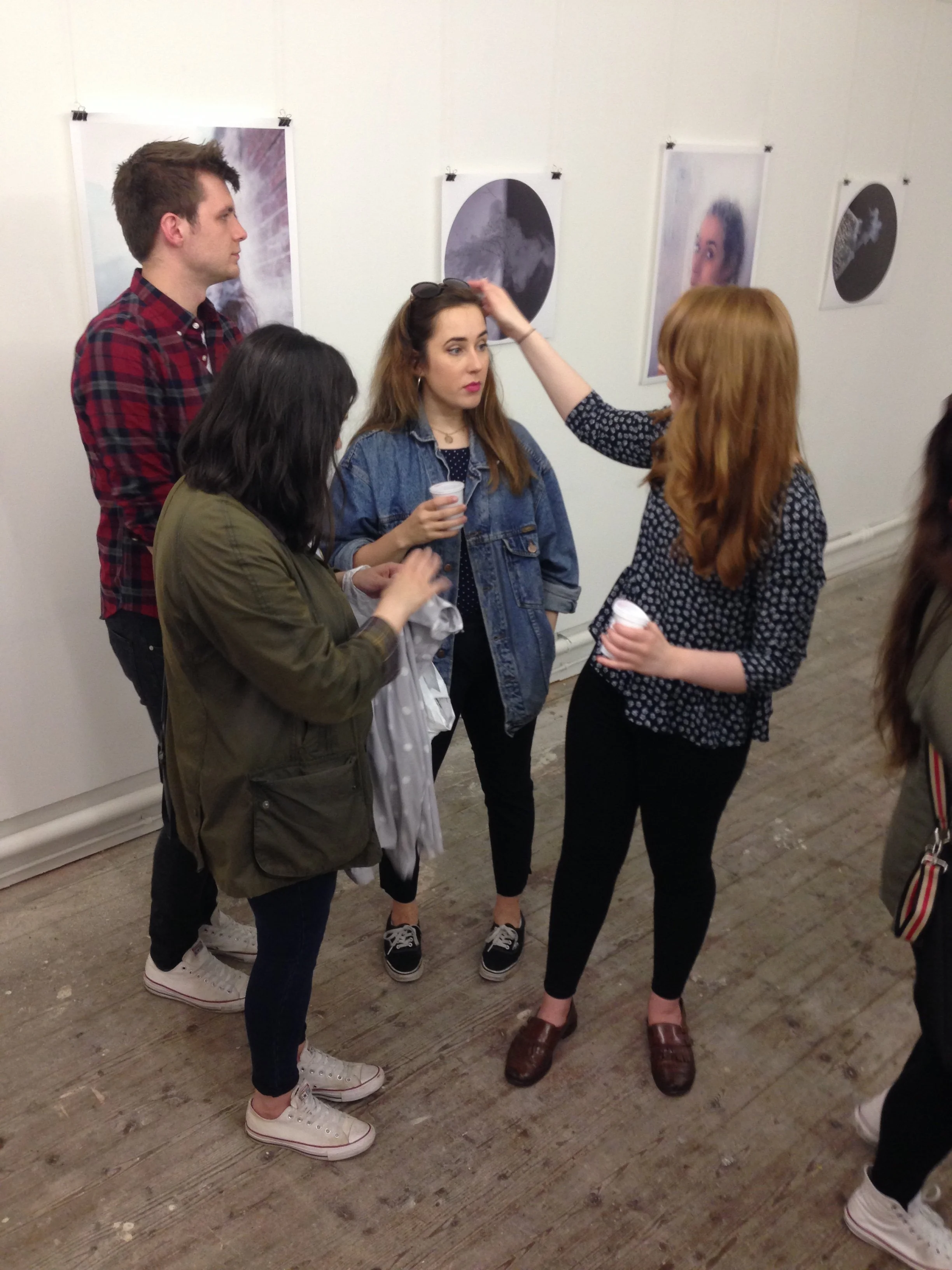 Group of women and a man standing in an art gallery, talking and looking at each other, with abstract art on the wall behind them.