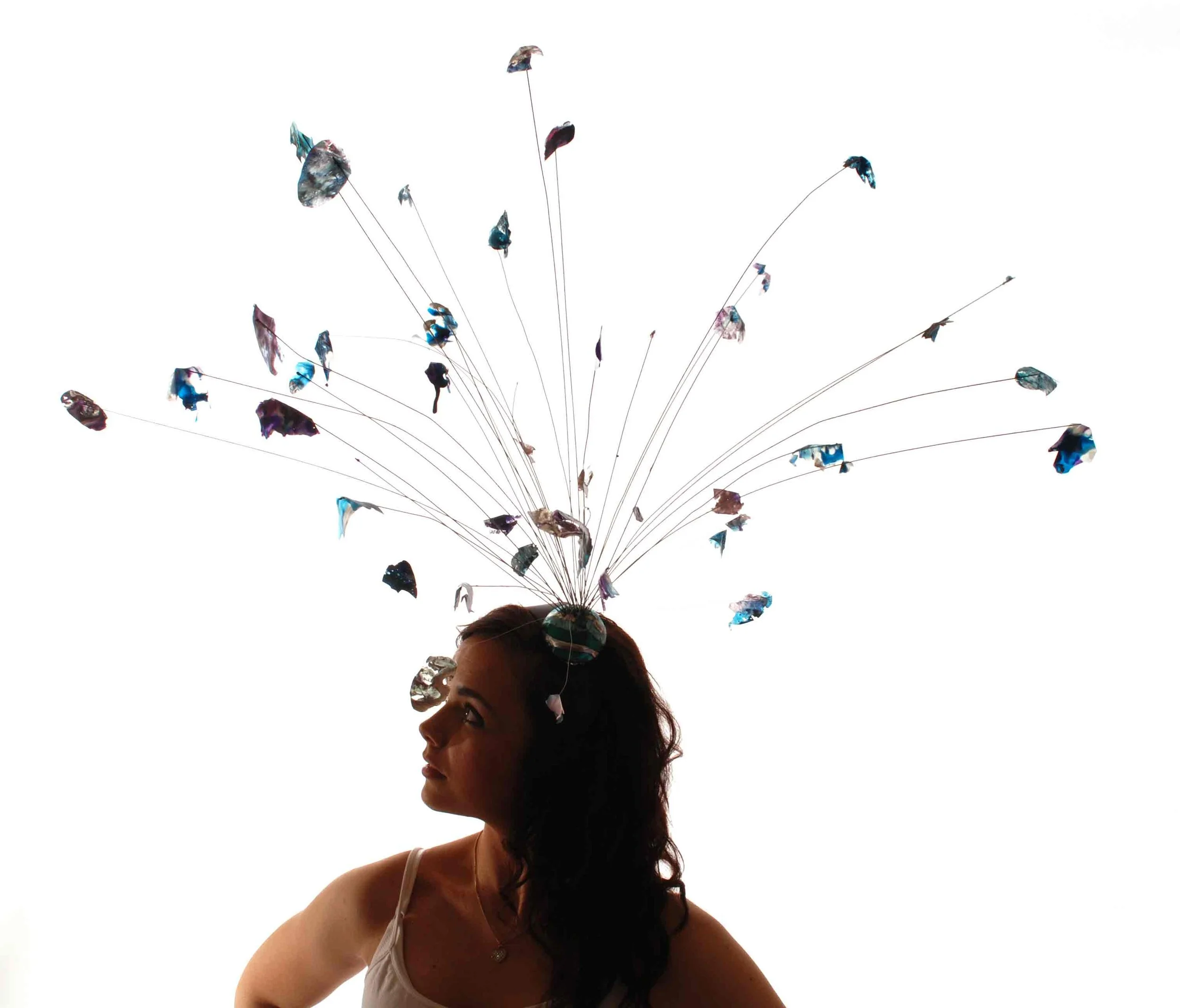 A woman with long dark hair and a white tank top is looking to her right, wearing a headpiece that resemble confetti.