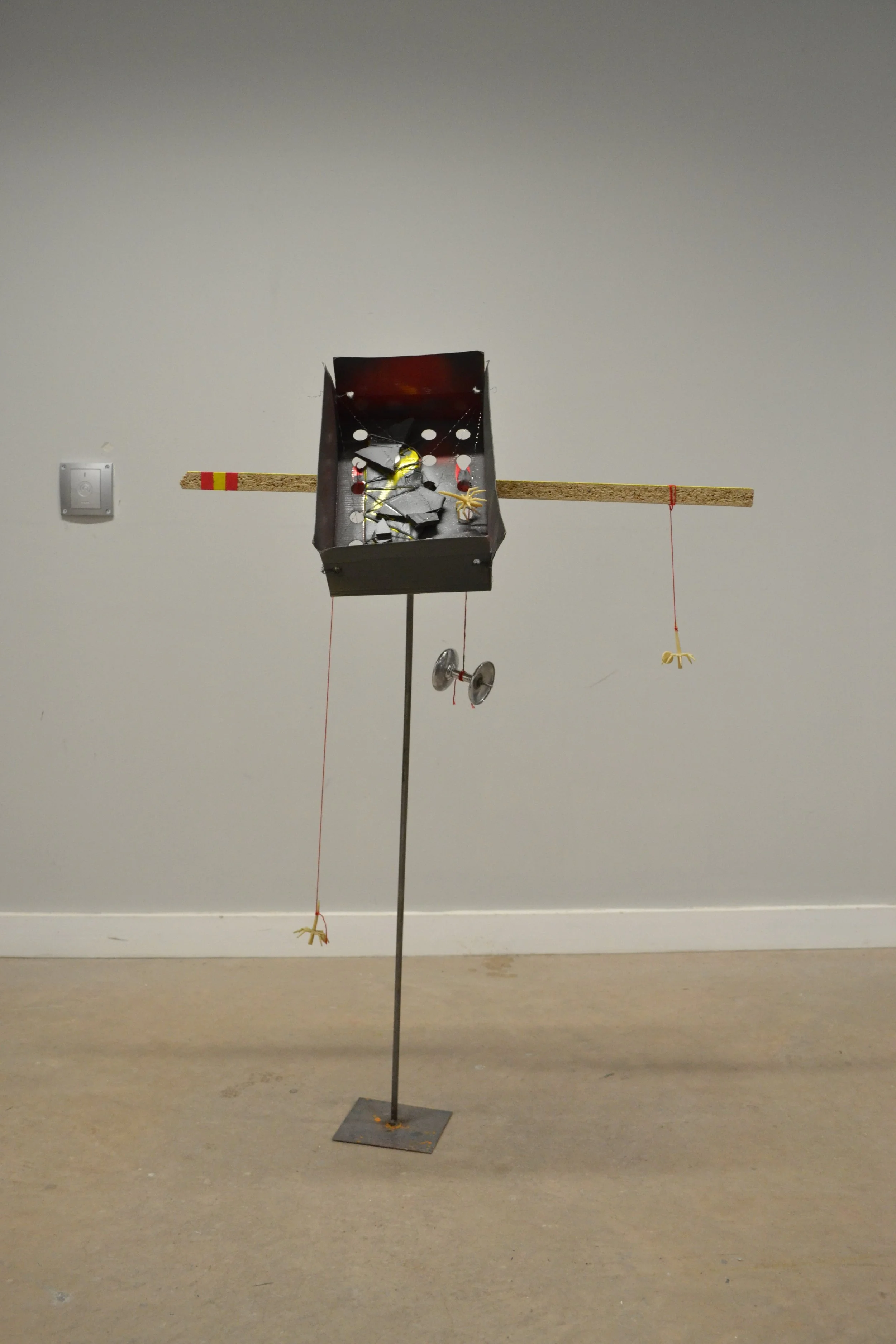 A small homemade device resembling a bird feeder or small weather station, mounted on a metal pole in a room with beige carpet and white walls.