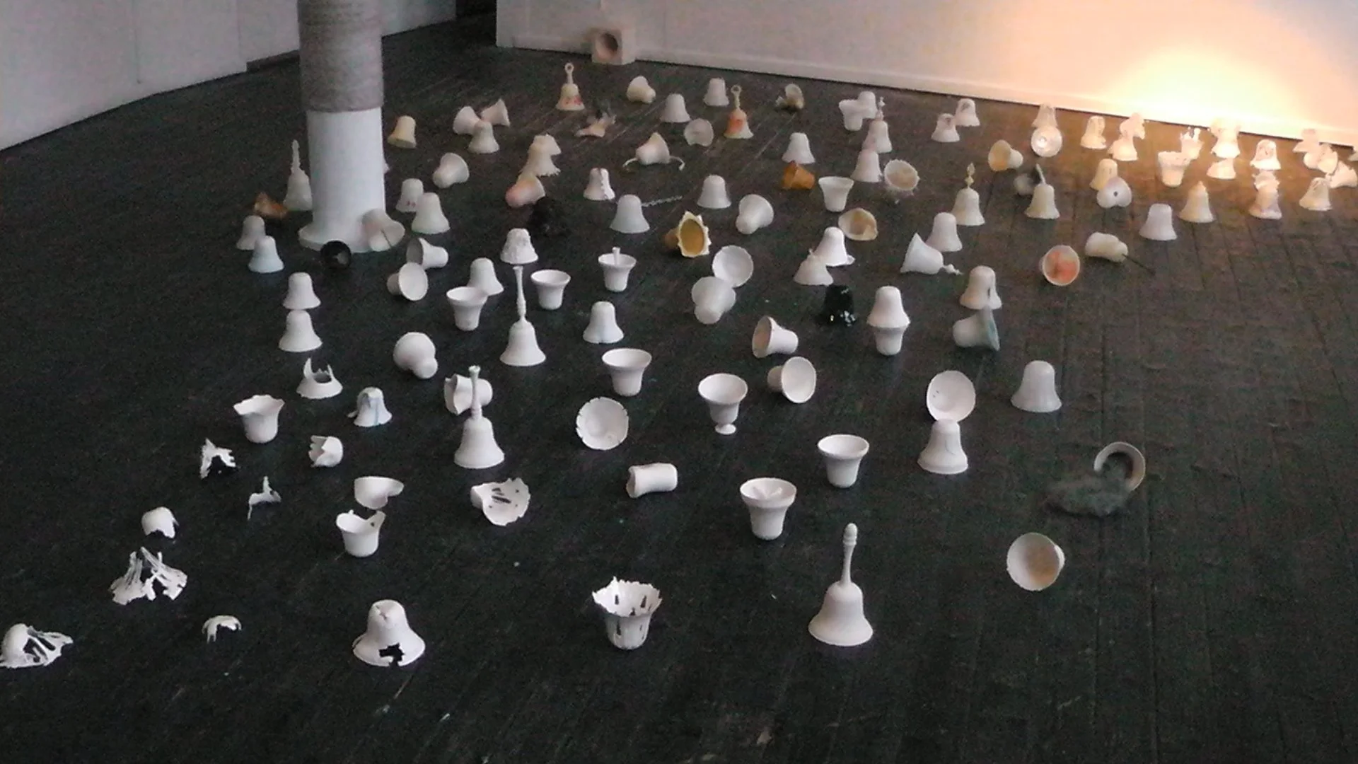 Broken white plastic cups scattered on dark floor with a large white pipe and a wall in the background, illuminated by a light source on the right.