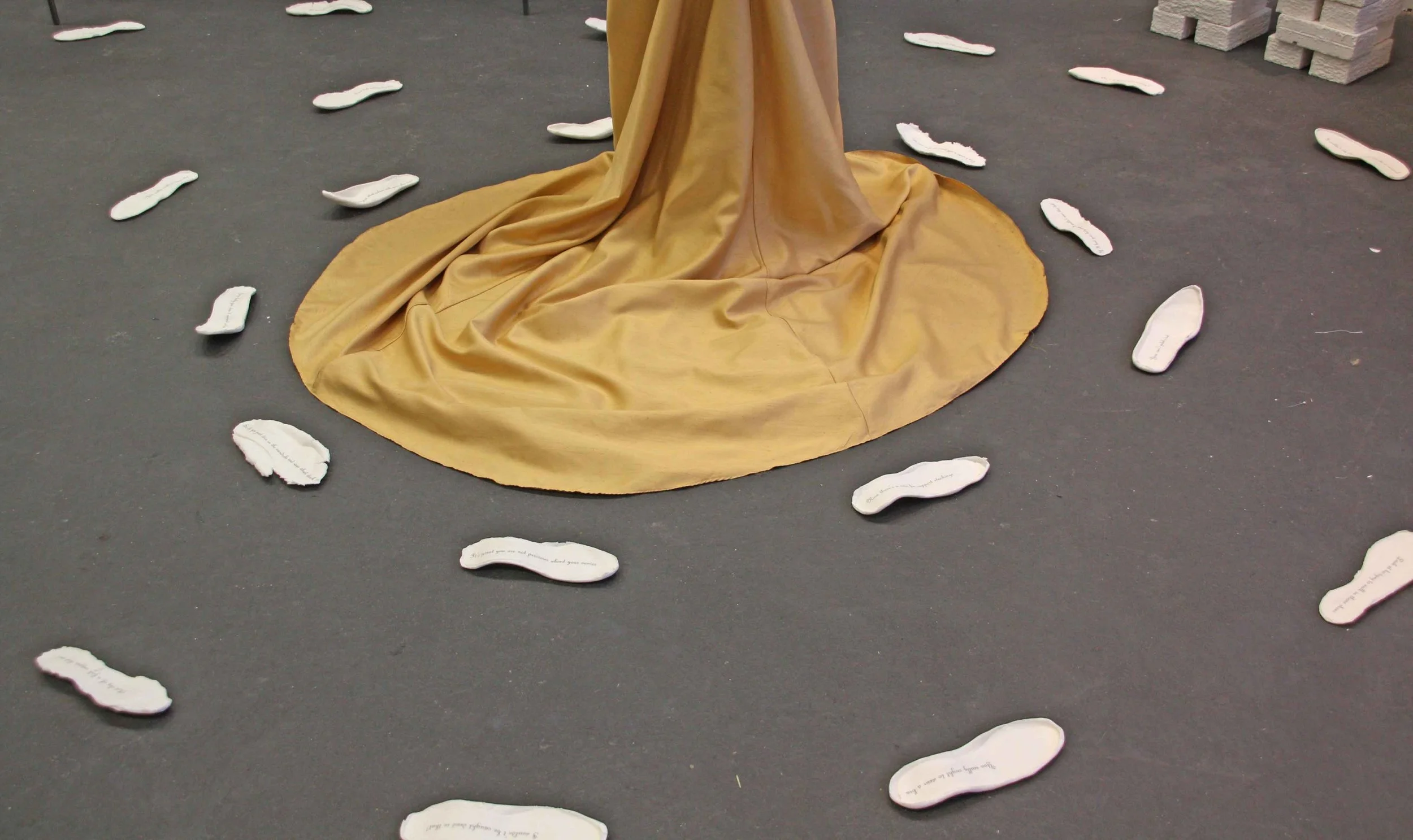 A golden-colored fabric drapes on the floor surrounded by white paper cutouts with handwritten text on a dark surface.