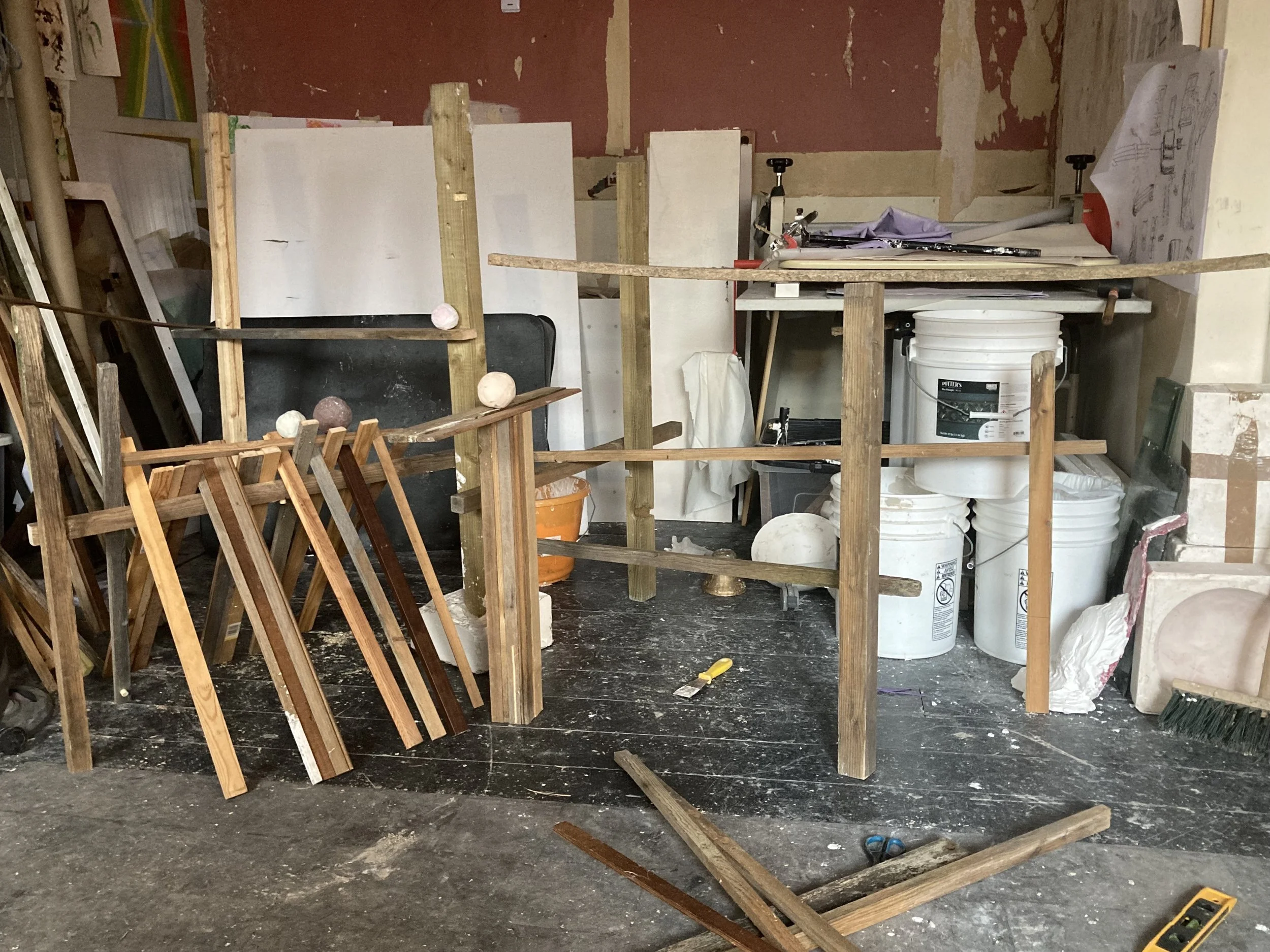 Construction or renovation art installation with wooden framing, white buckets, tools, and background wall with peeling paint.