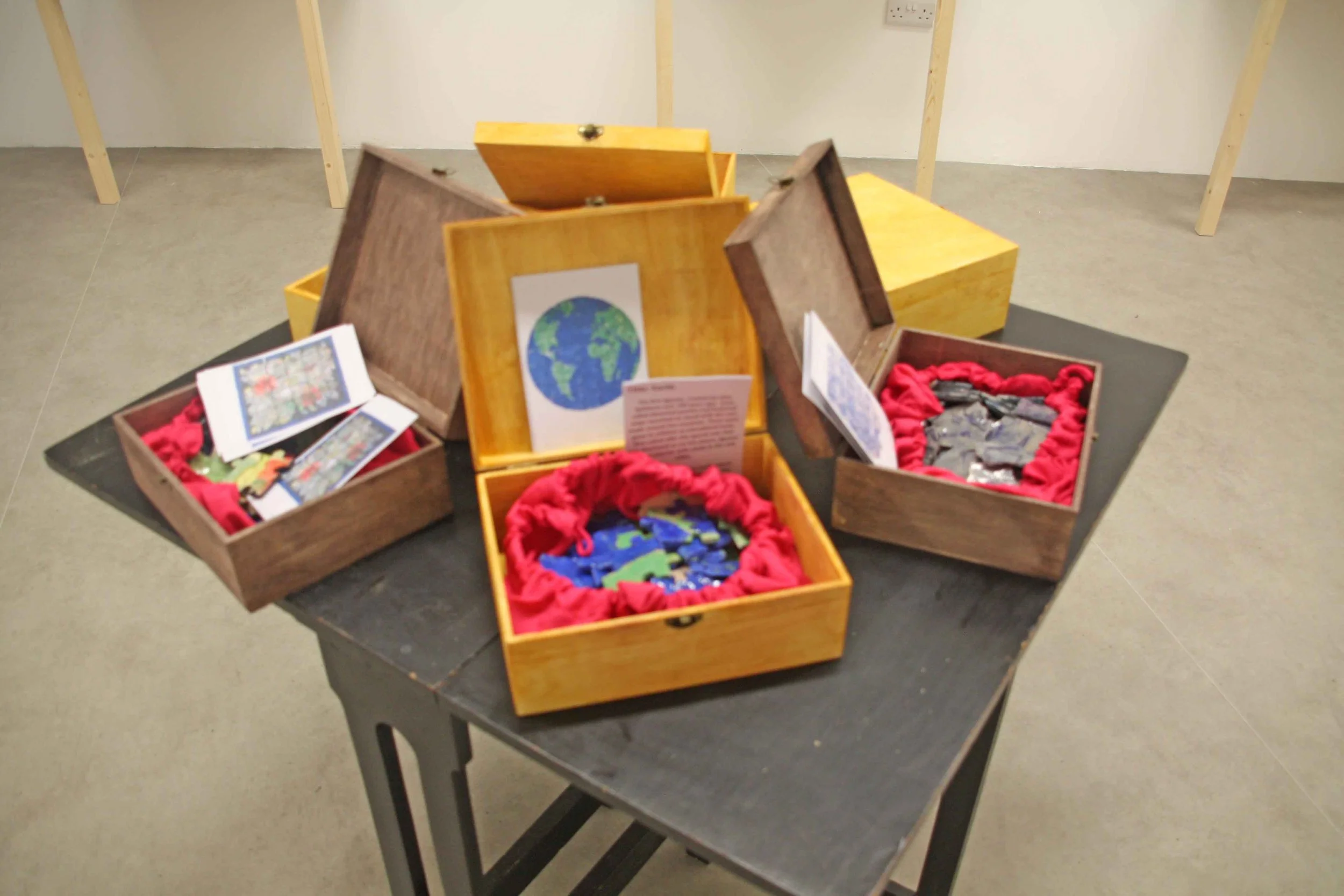 Display of open wooden boxes containing puzzles and small objects on a black table, with a plain wall and floor in the background.