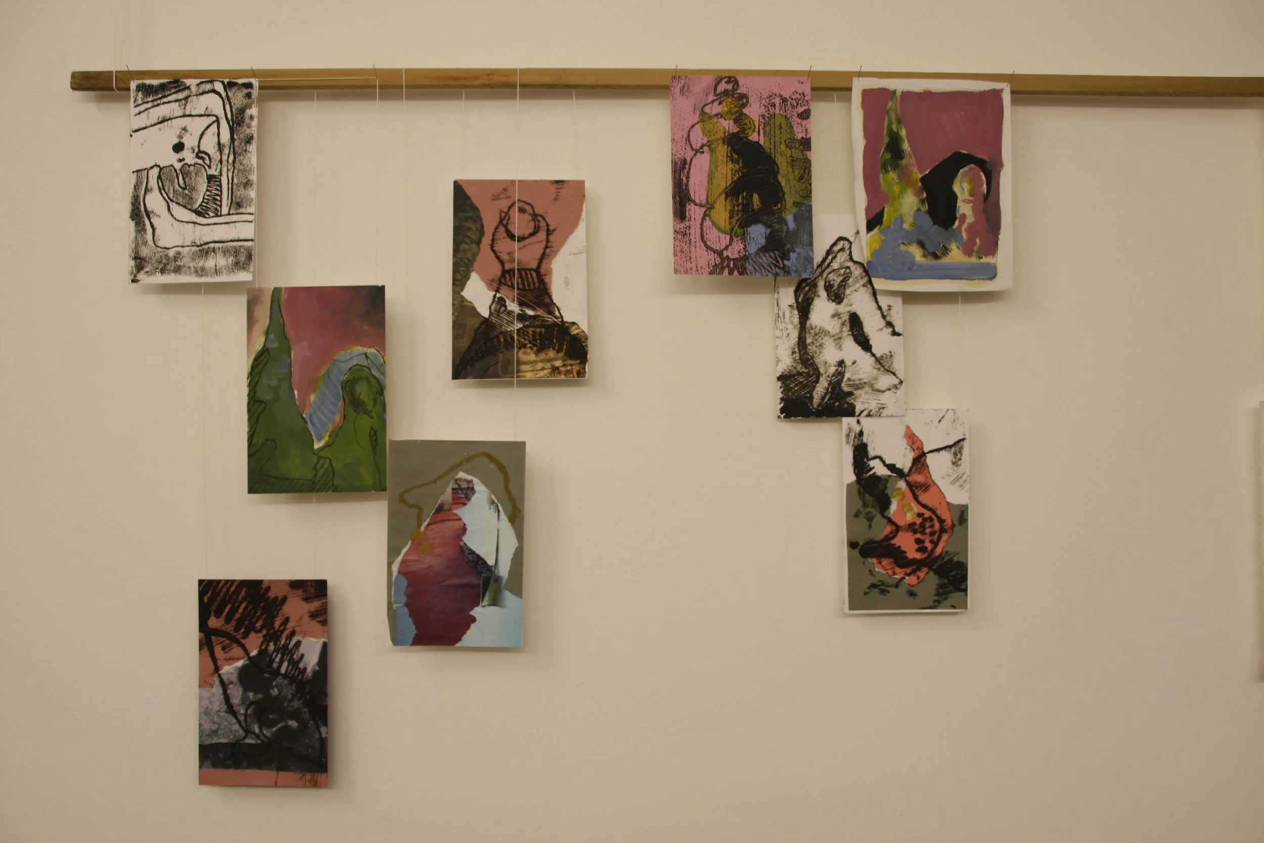 A wall display of abstract art pieces hanging from a wooden rod, featuring various colors and brushstroke styles.