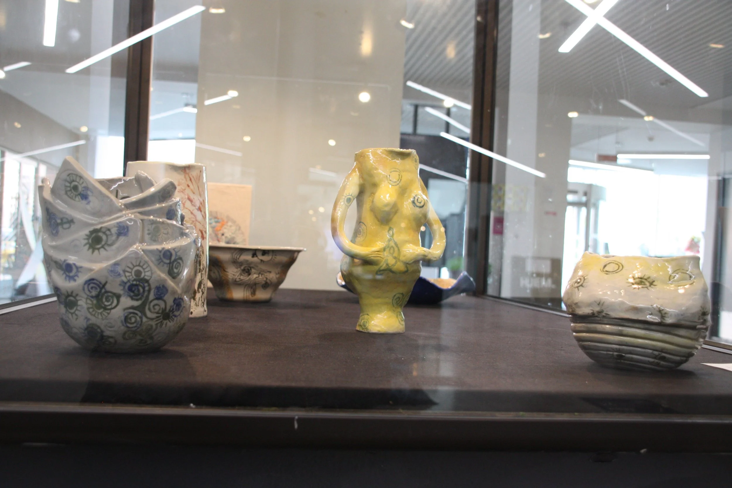 Various ceramic vases and sculptures on display in a glass case at a museum or gallery, with modern lighting overhead.