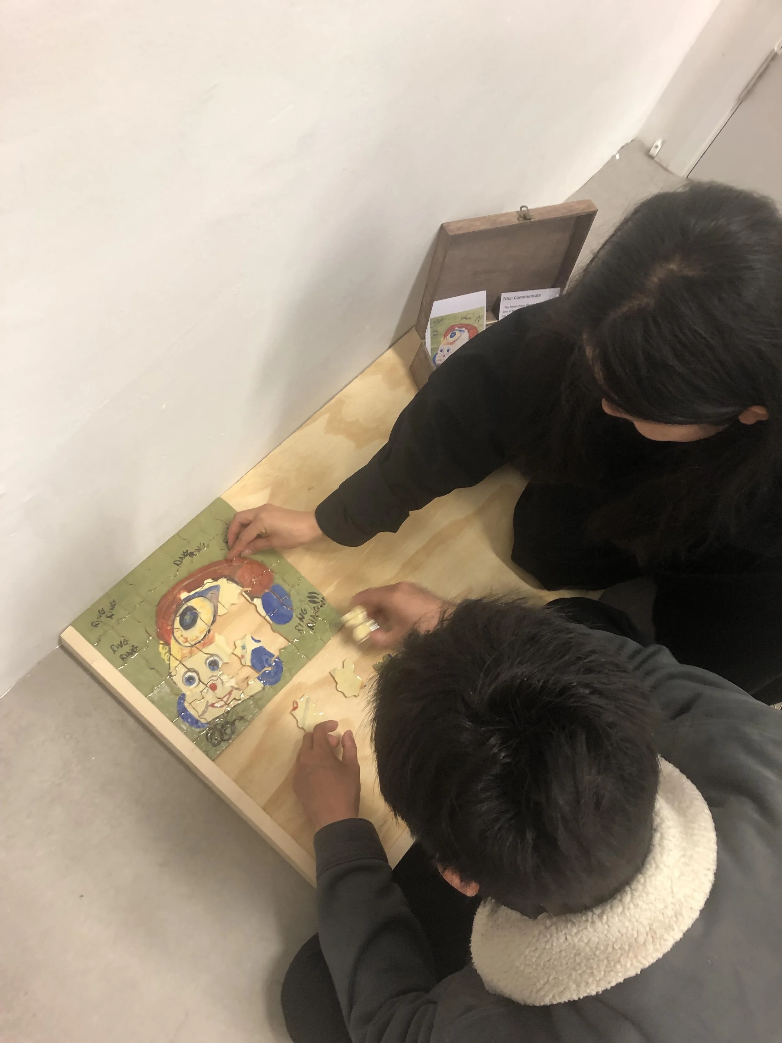 Two people are working together on assembling a jigsaw puzzle with a picture of a cartoon character on a wooden table, in an indoor setting.