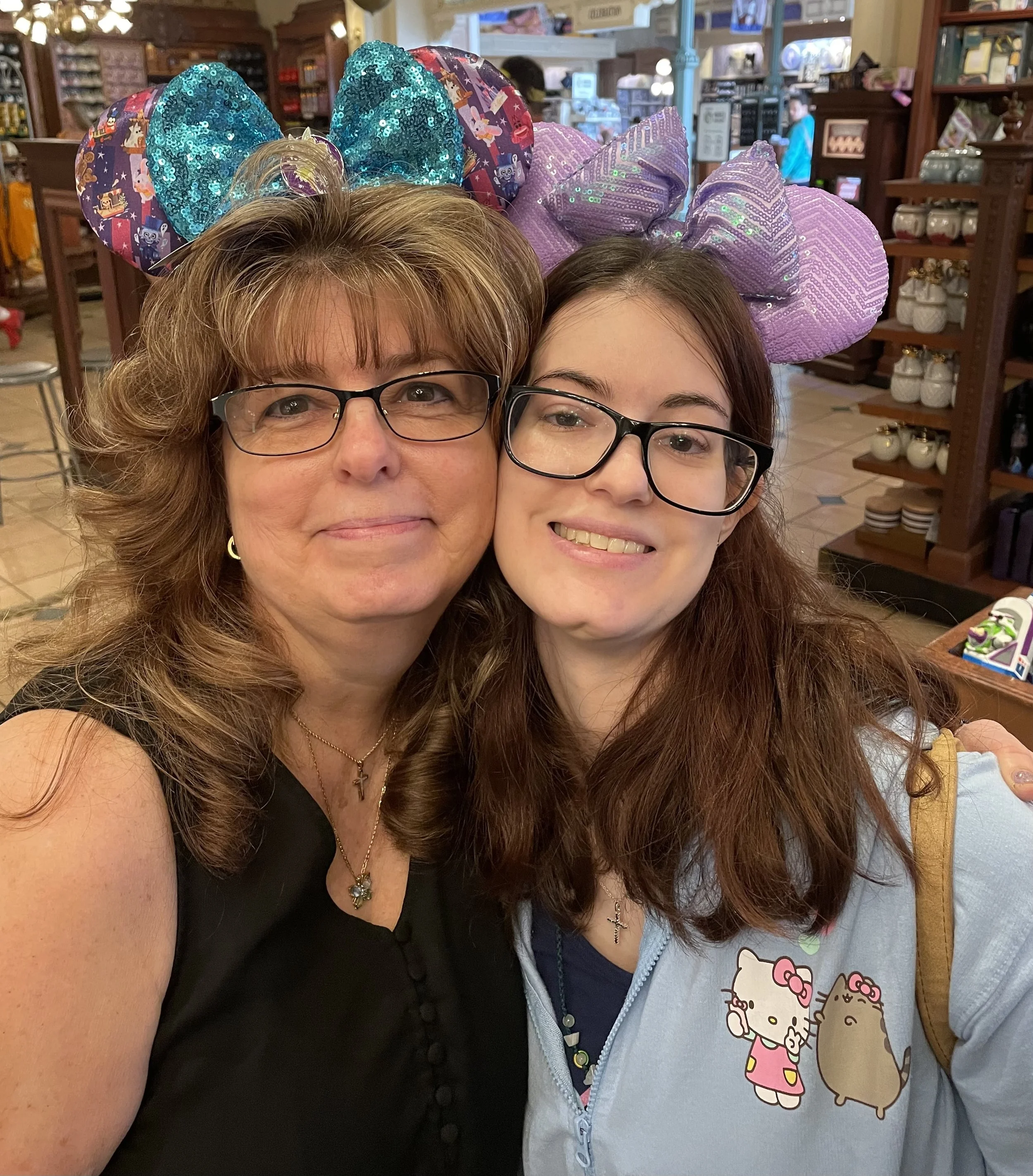 Two women taking a selfie with Minnie Mouse ears headbands, with jewelry and glasses, inside a store with shelves of items in the background.