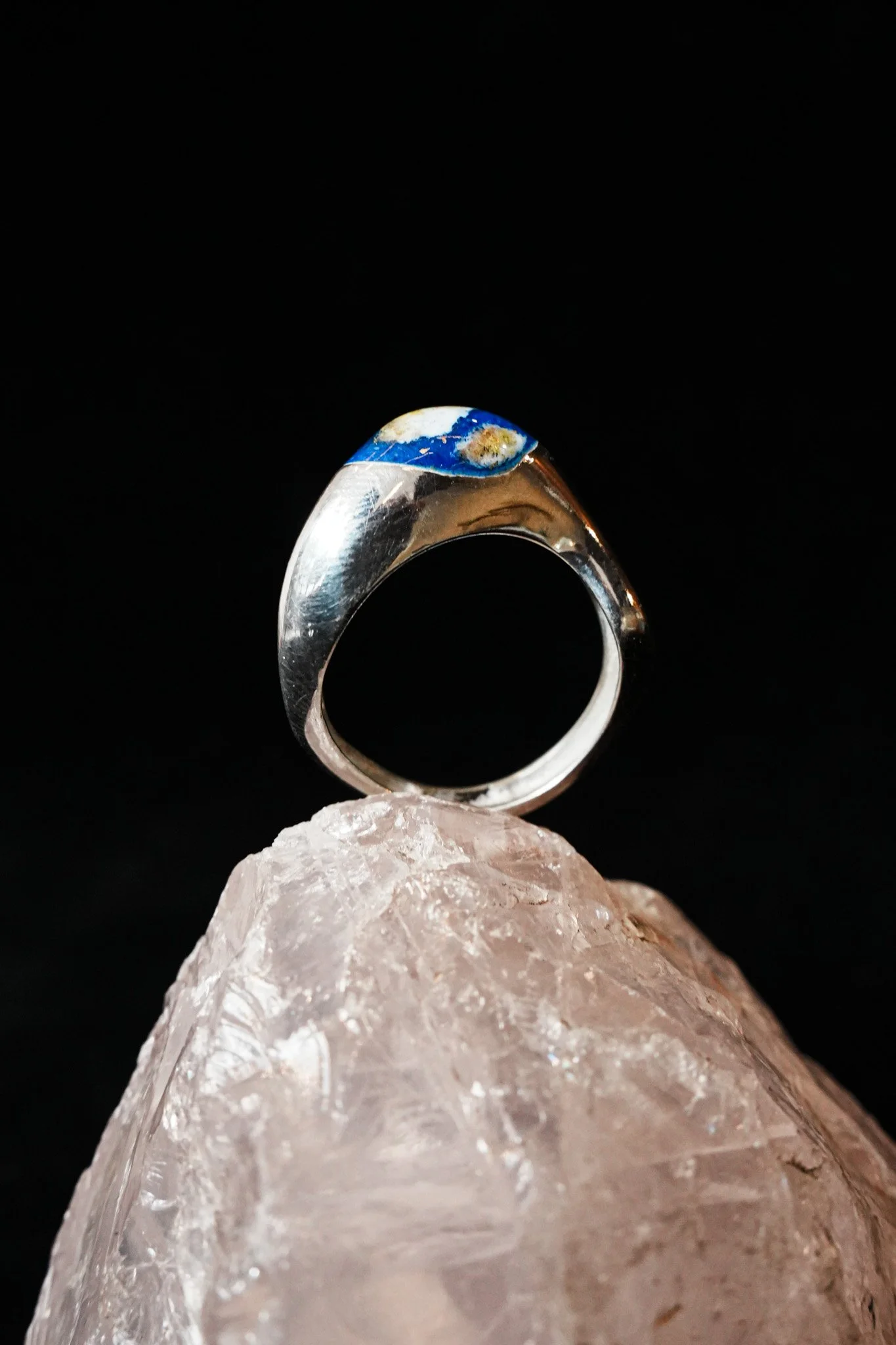 Un anillo de plata con detalles en azul, colocado sobre una piedra de cuarzo rosa.