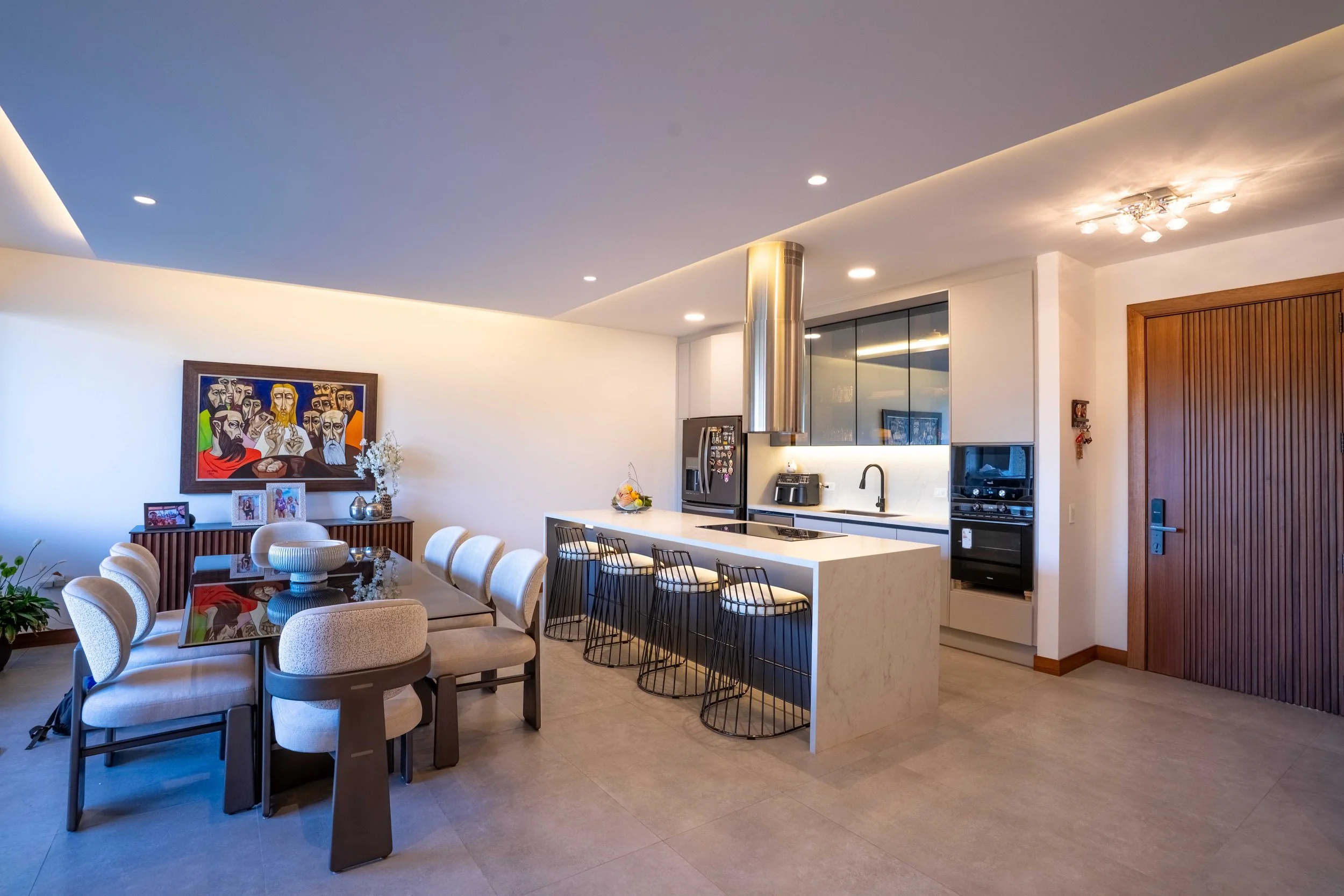Interior moderno de cocina y comedor con muebles blancos, sillas blancas y negras, arte en la pared y electrodomésticos de acero inoxidable.