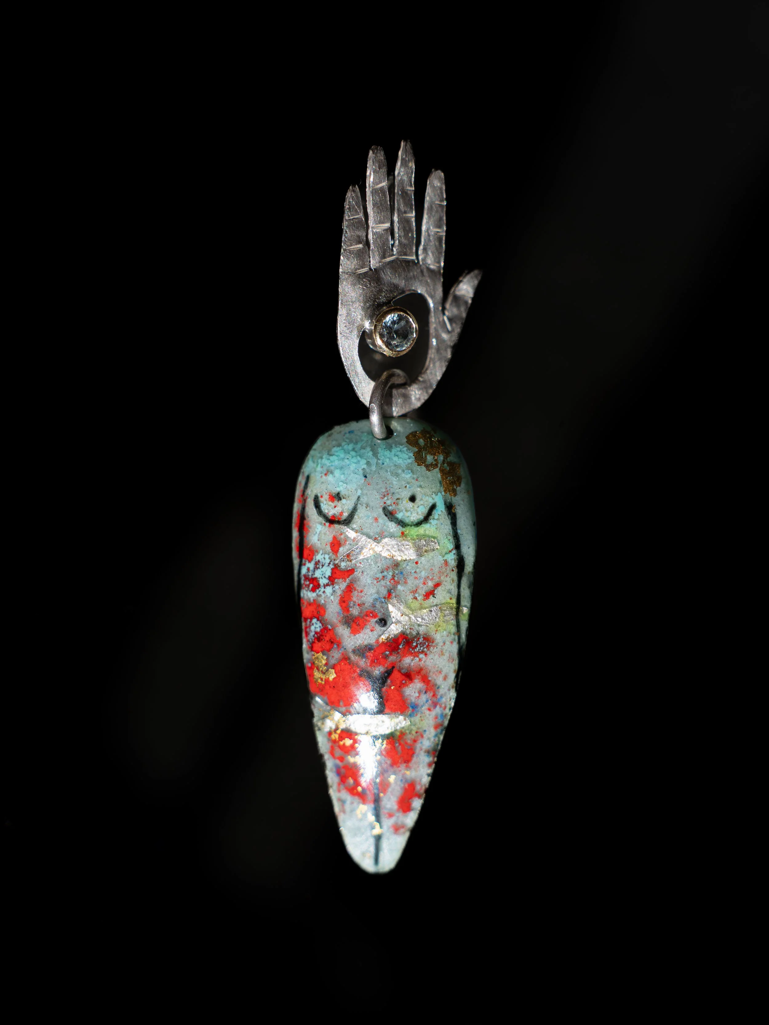 Pulsera con un colgante que tiene una figura de una cara con ojos cerrados, decorada con colores y patrones pintados a mano.