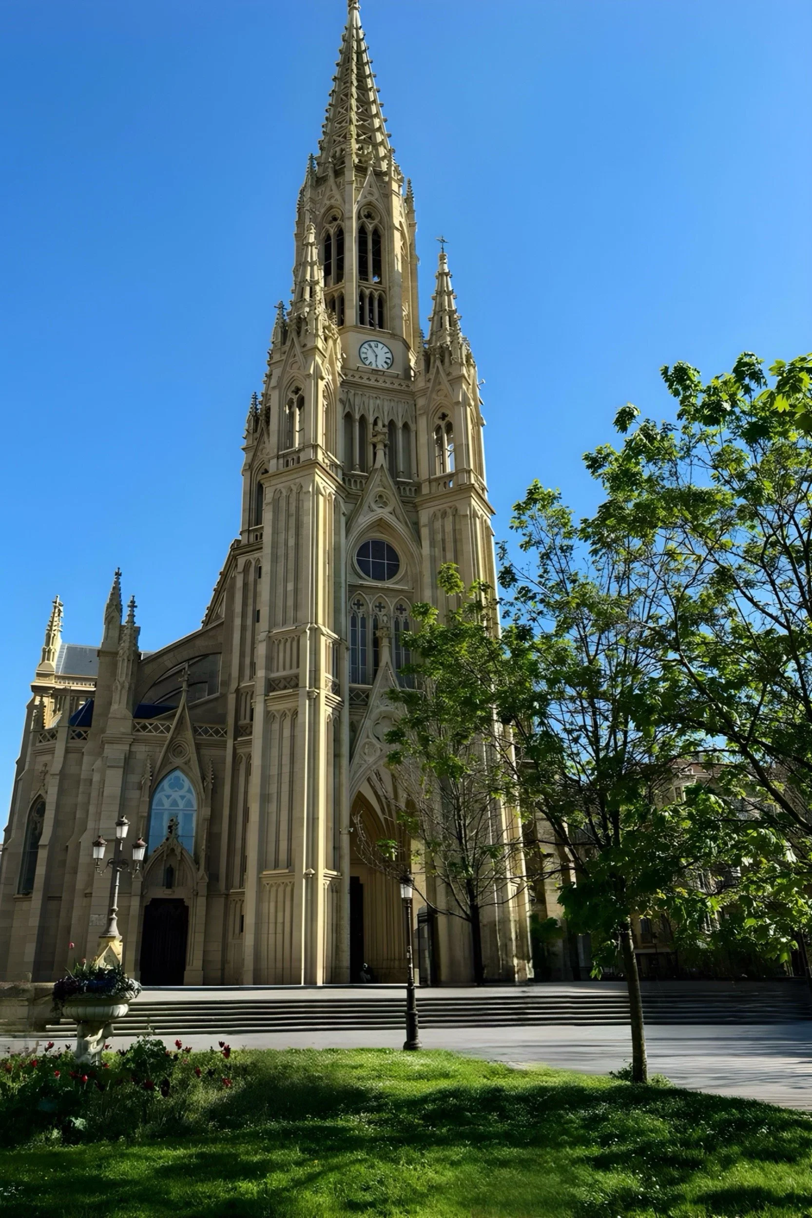 The impressive Neo-Gothic facade and soaring needle spire of the Cathedral of the Good Shepherd in San Sebastián, Spain, viewed from a sunny courtyard