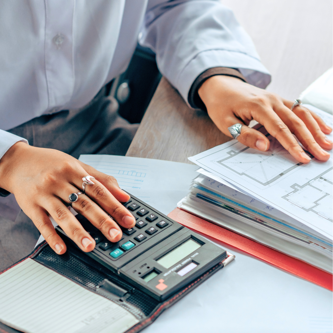Person using calculator and reviewing architectural plans on a desk.