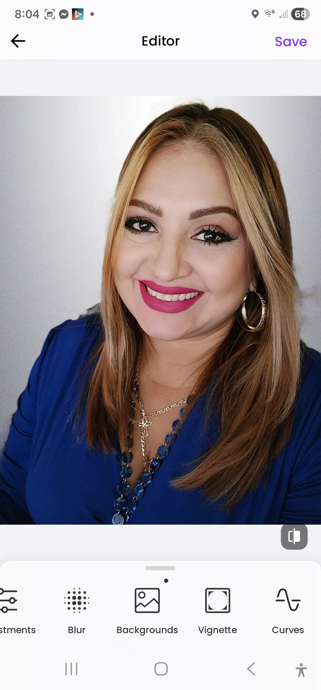 A woman smiling, wearing a blue top and gold jewelry, with long brown hair and large hoop earrings.