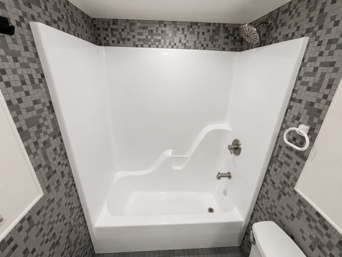 Bathroom shower with gray mosaic tile walls, white shower surround, shower head, and a toilet to the right.
