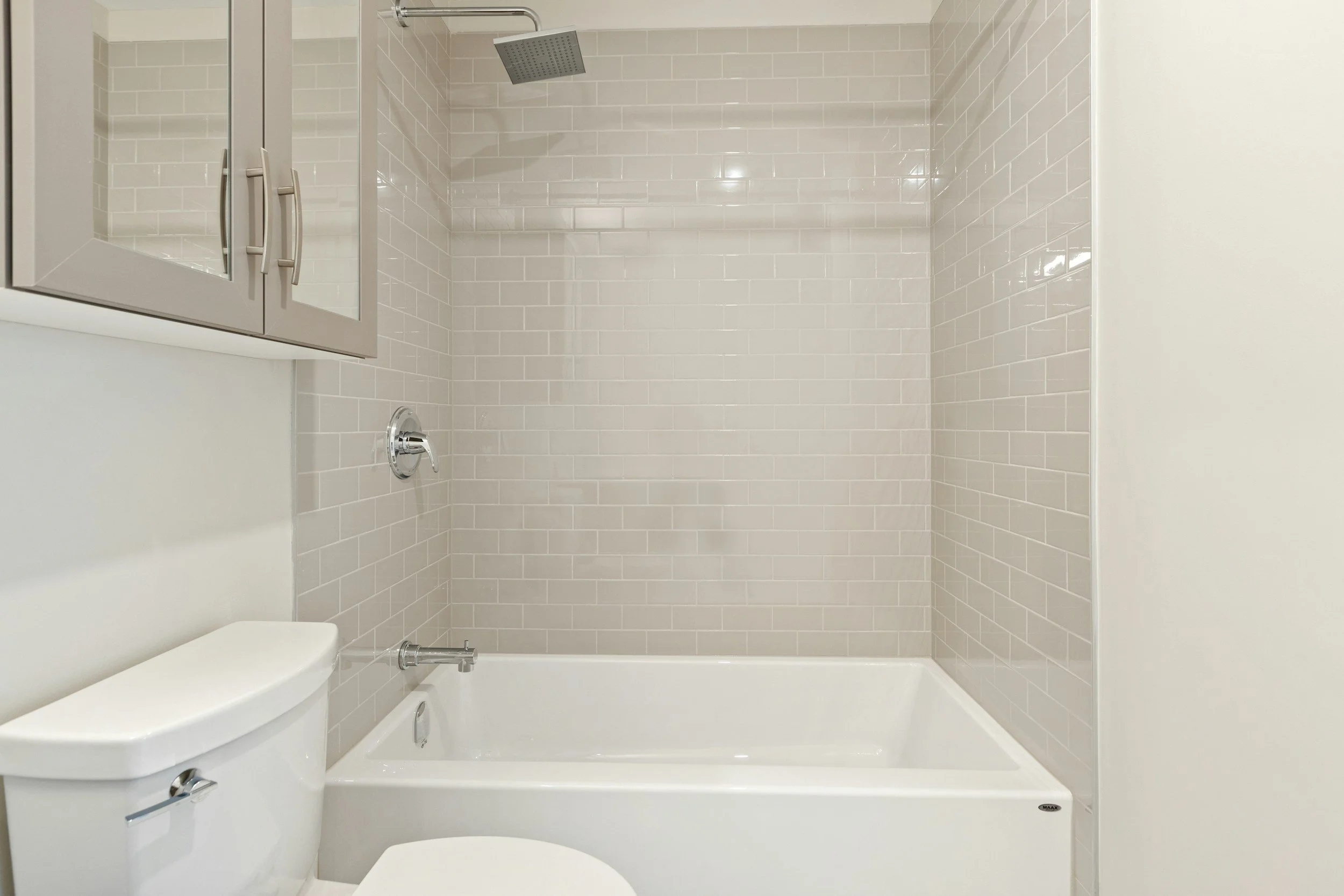 Bathroom with light-colored tile walls, a showerhead, a bathtub, and a mirrored cabinet.