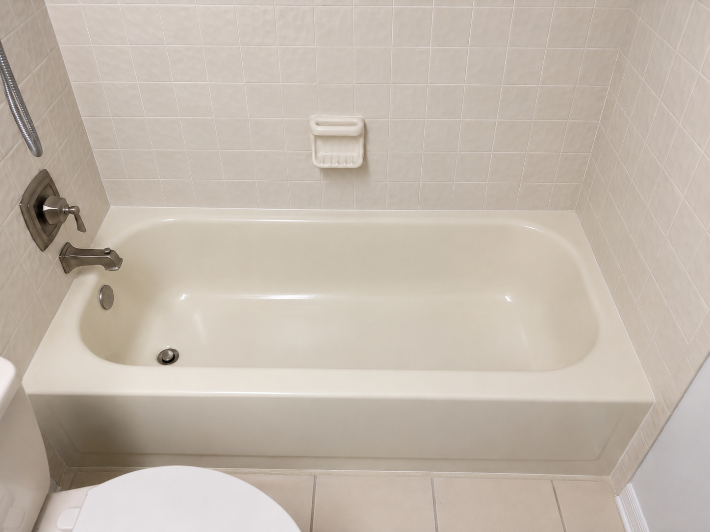 Empty bathtub in a bathroom, with tiled walls, a soap holder, and a showerhead on the left side.