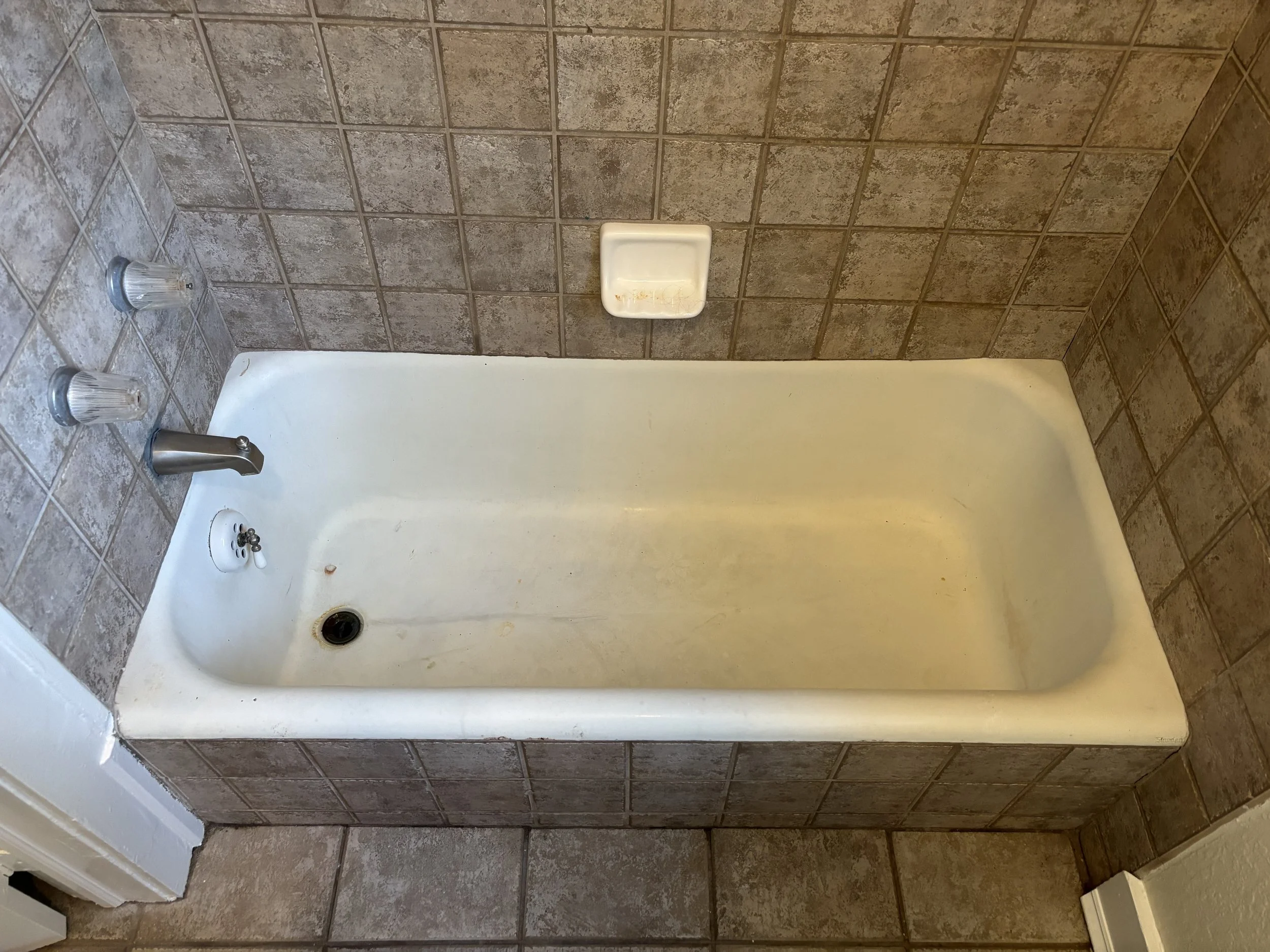 Bathroom shower with brown tiled walls, a soap dish, and two shower knobs.