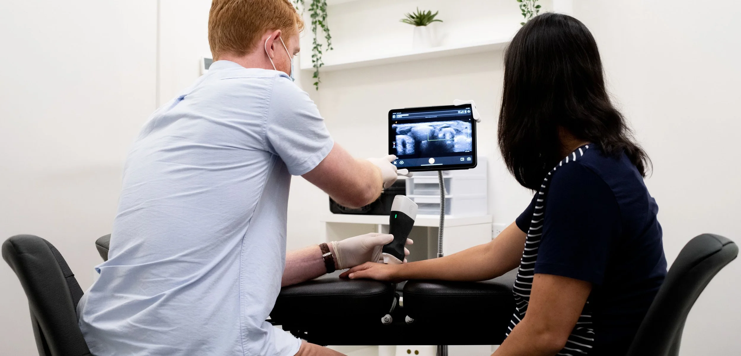 A healthcare professional showing a medical ultrasound scan on a tablet to a female patient in a clinical setting.