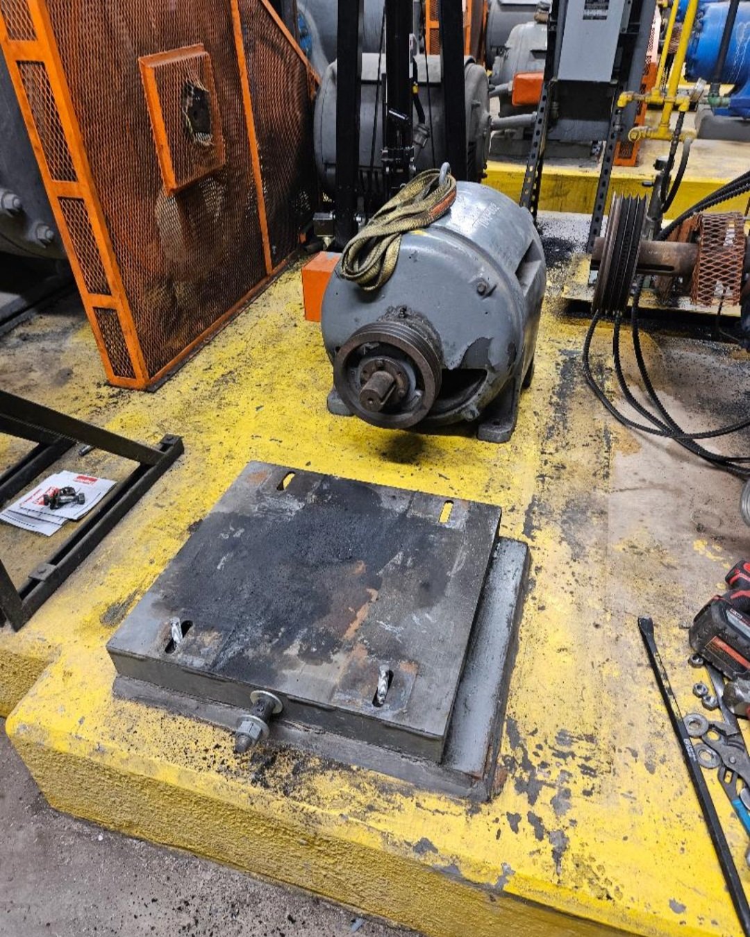 Industrial workshop with a large gray electric motor on a yellow workbench, surrounded by tools, parts, and equipment.