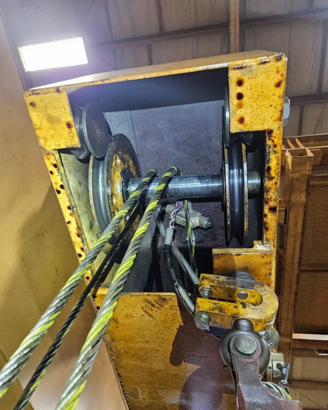Close-up of a yellow industrial lifting or hoisting mechanism with steel cables and pulleys, showing signs of rust and wear.