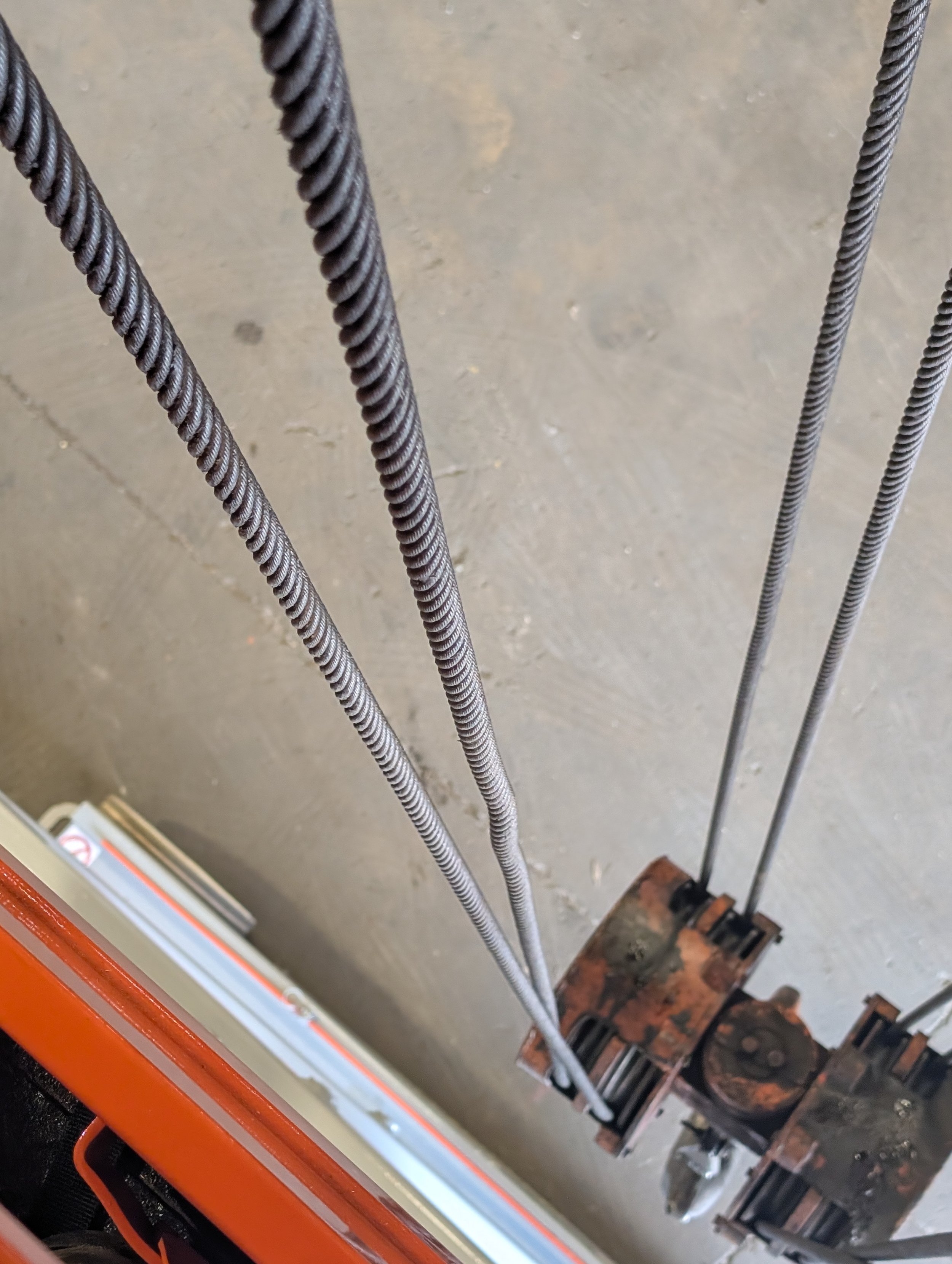 Close-up view of three steel rebar rods in a construction setting, with a rusty pipe and concrete floor visible in the background.