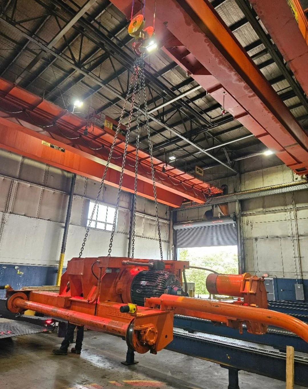 Large industrial machine being installed or maintained inside a factory or warehouse, with a large overhead crane lifting or supporting it.