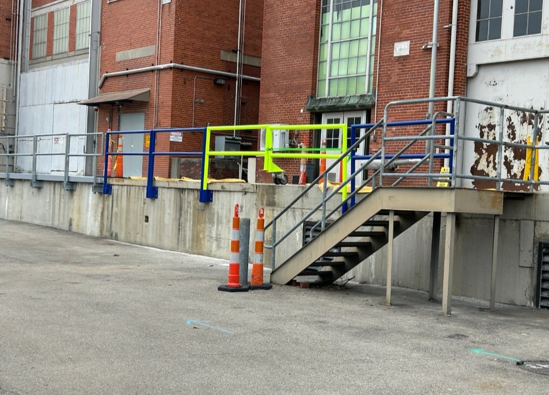 A temporary construction barrier with colorful railings and orange safety cones in front of a building with brick and metal siding.