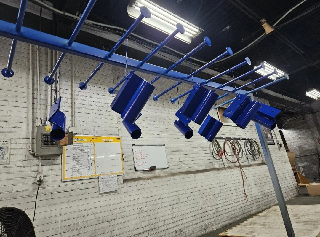 Blue wall-mounted coat rack with multiple hooks hanging down in a workshop or industrial space.