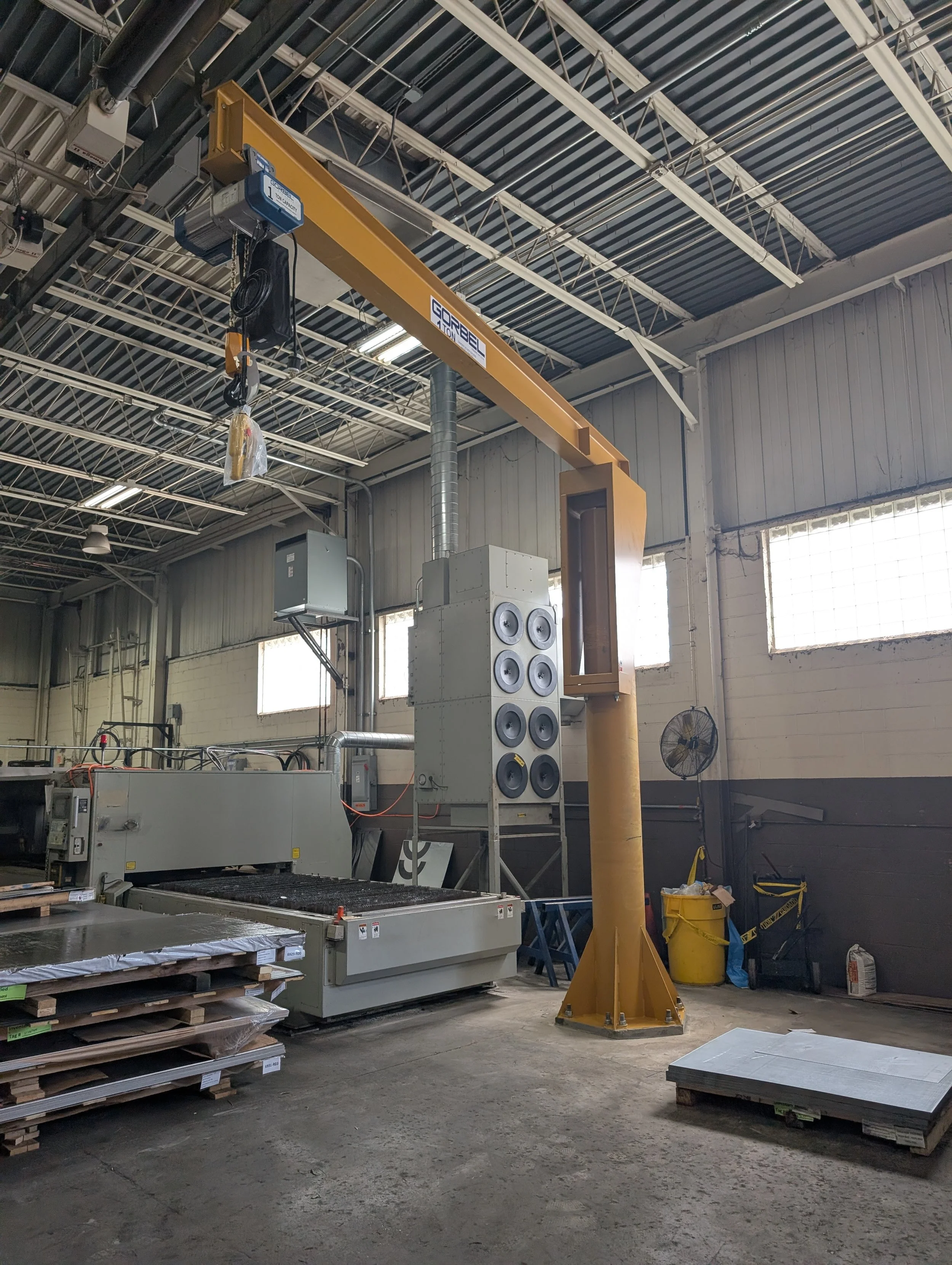 Industrial warehouse with a yellow overhead crane, storage racks, and stacks of materials on pallets.