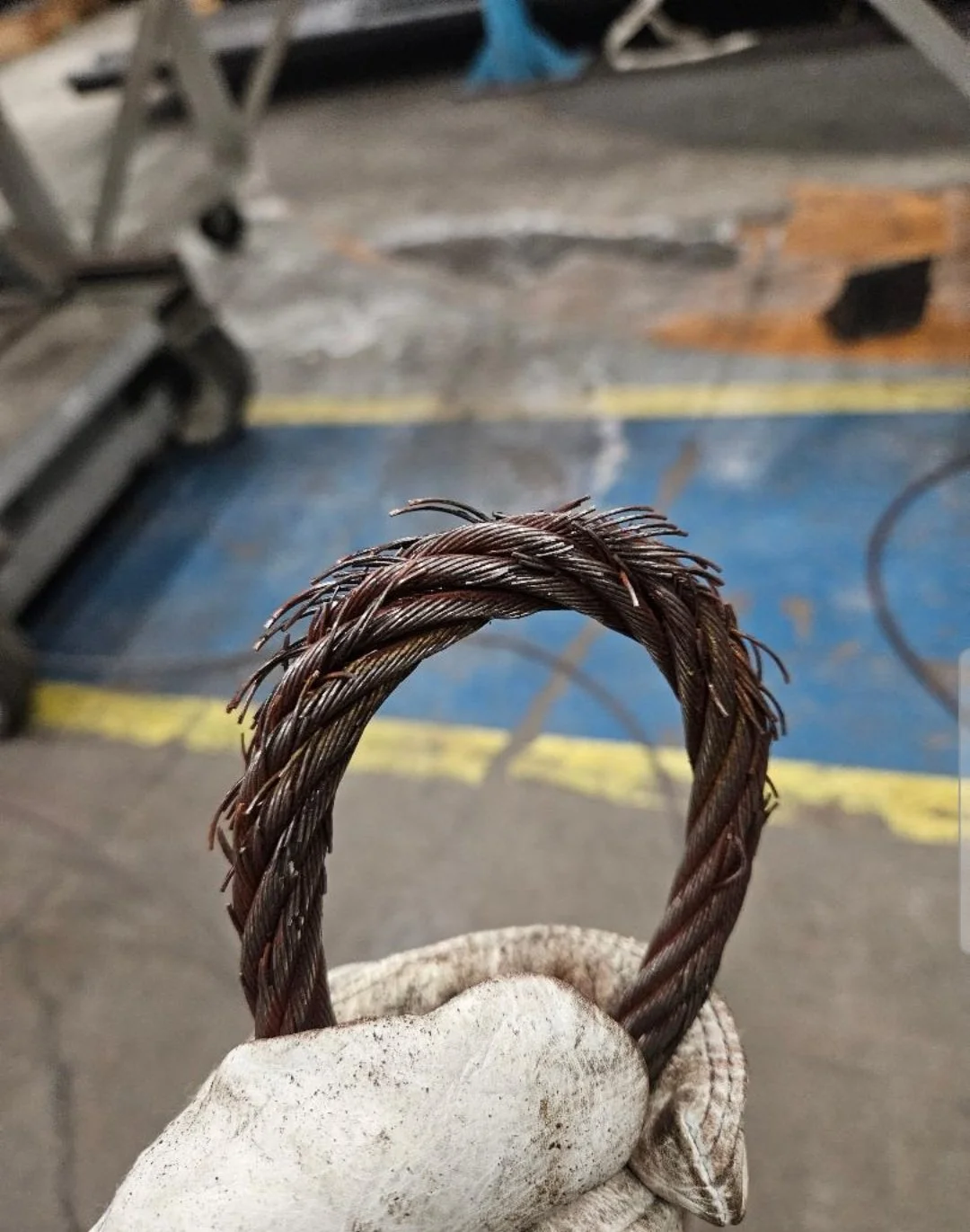 Close-up of a frayed steel wire rope held by a gloved hand in a workshop setting.