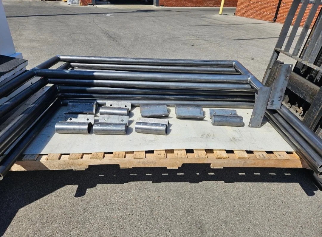 Metal pipes and fittings arranged on a wooden pallet at an outdoor location.