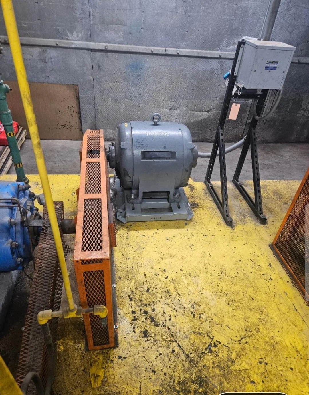 Industrial machine in a factory setting with yellow floor and gray and orange safety barriers.