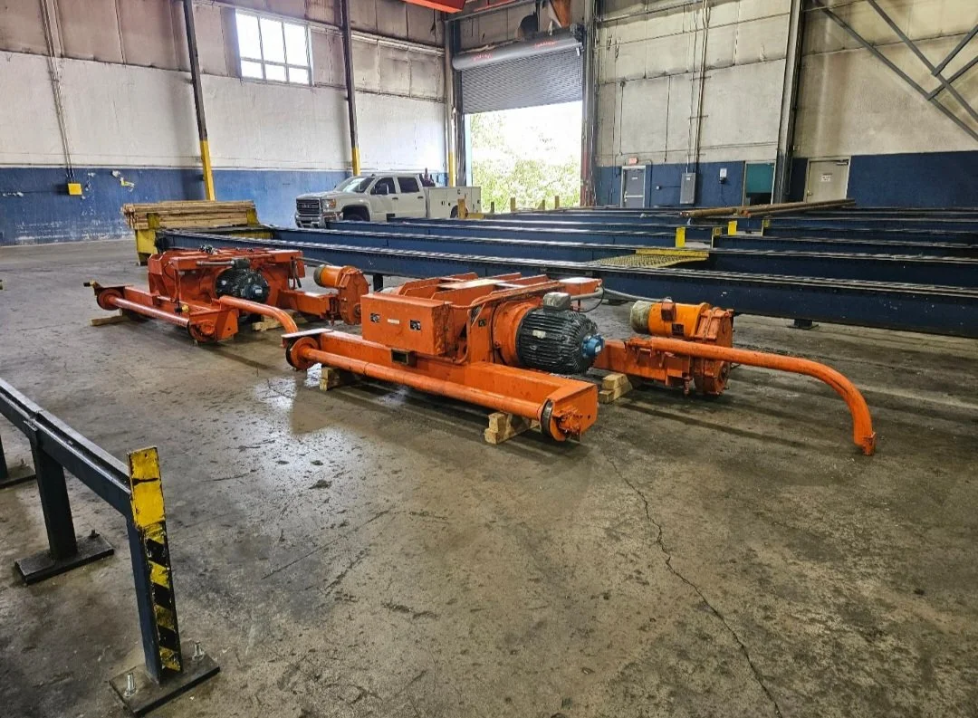 Industrial machinery with orange motors and pipes inside a warehouse, with a truck and blue metal beams in the background.