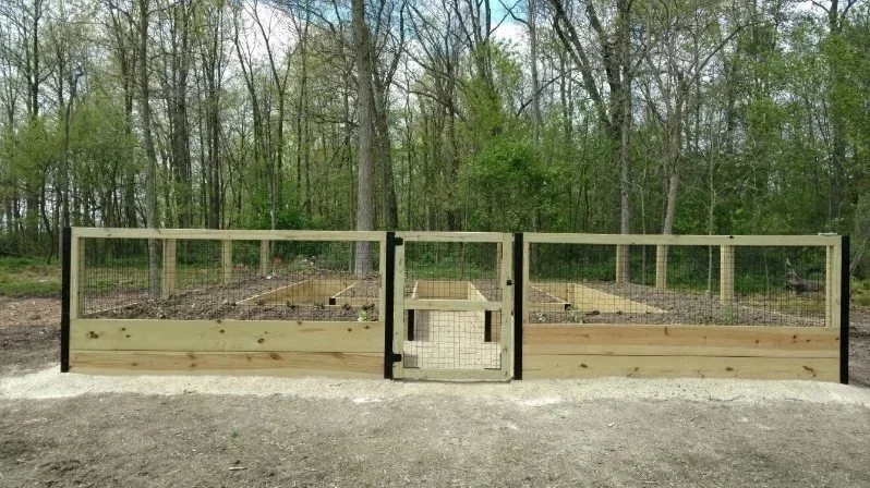 A fenced outdoor chicken coop with a wooden frame and wire mesh, located in a wooded area.