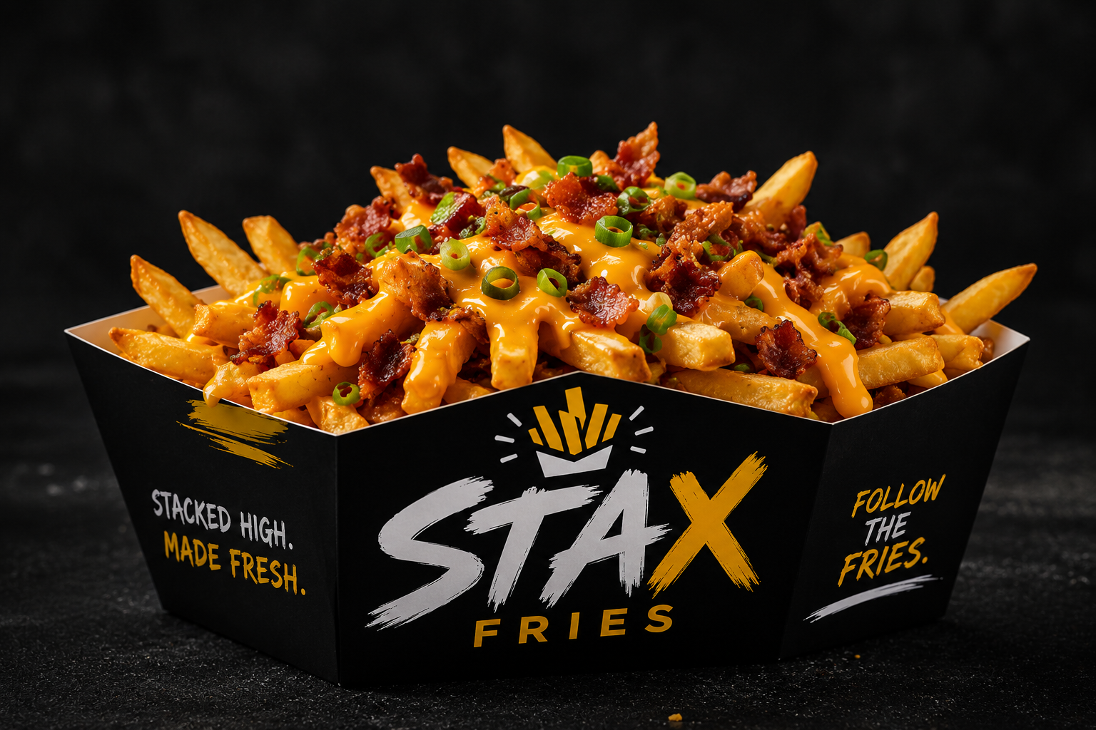 Tray of loaded French fries topped with cheese sauce, bacon bits, and chopped green onions in a black container with the label 'Stax Fries'.