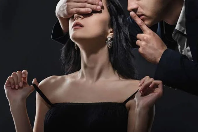 A woman with black hair and earrings is having her makeup or hair done, with a man attending to her in a professional setting.