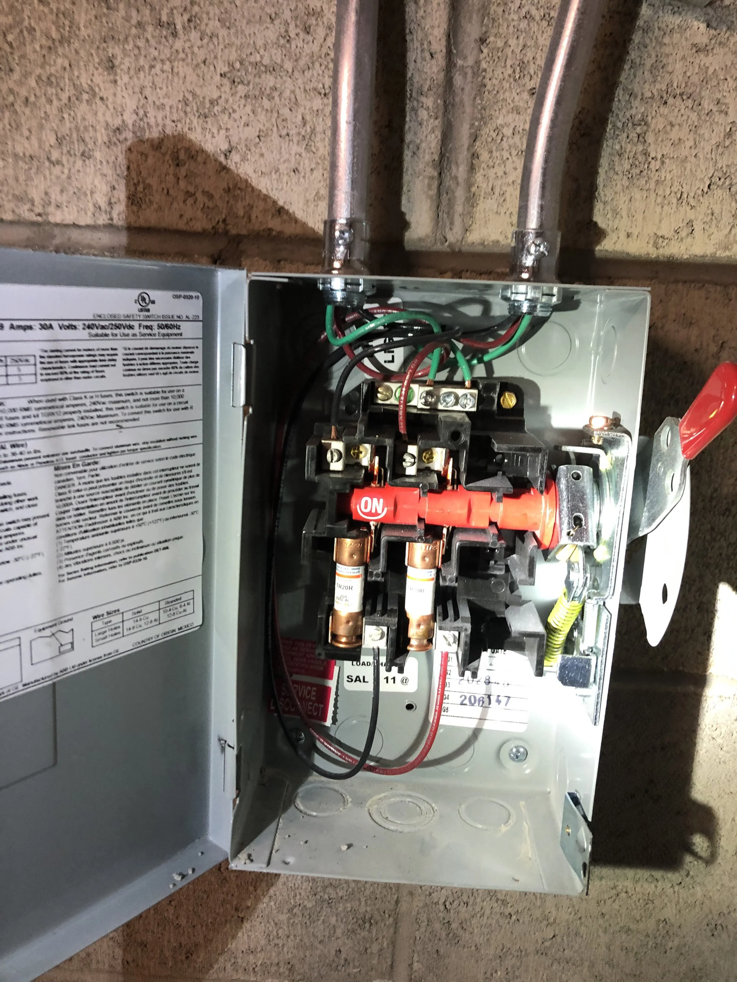 Open electrical panel with wiring and switches mounted inside metal enclosure.
