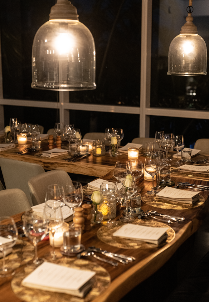 Elegant dining table set for a dinner party with wine glasses, candles, and floral arrangements in a dimly lit room.