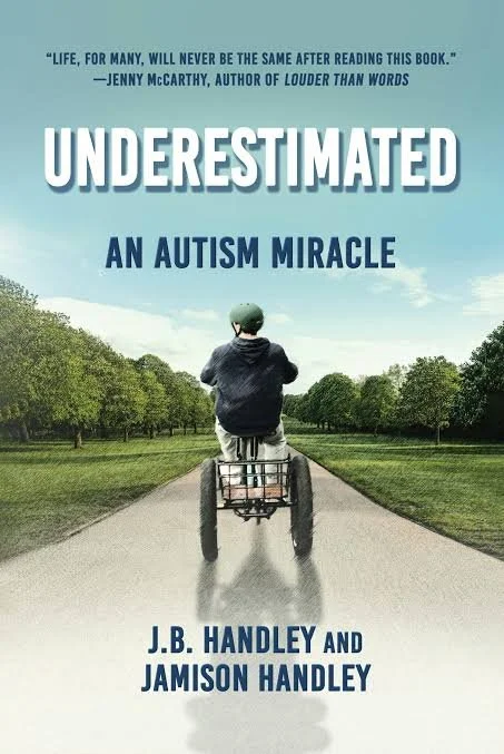 Book cover titled "Underrated: An Autism Miracle" by J.B. Handley and Jamison Handley. Features a child in a green helmet riding a tricycle on a paved path through a grassy park with trees and a partly cloudy sky.