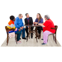 Six people seated around a small wooden table engaged in conversation, with a white rug underneath and a dark background.