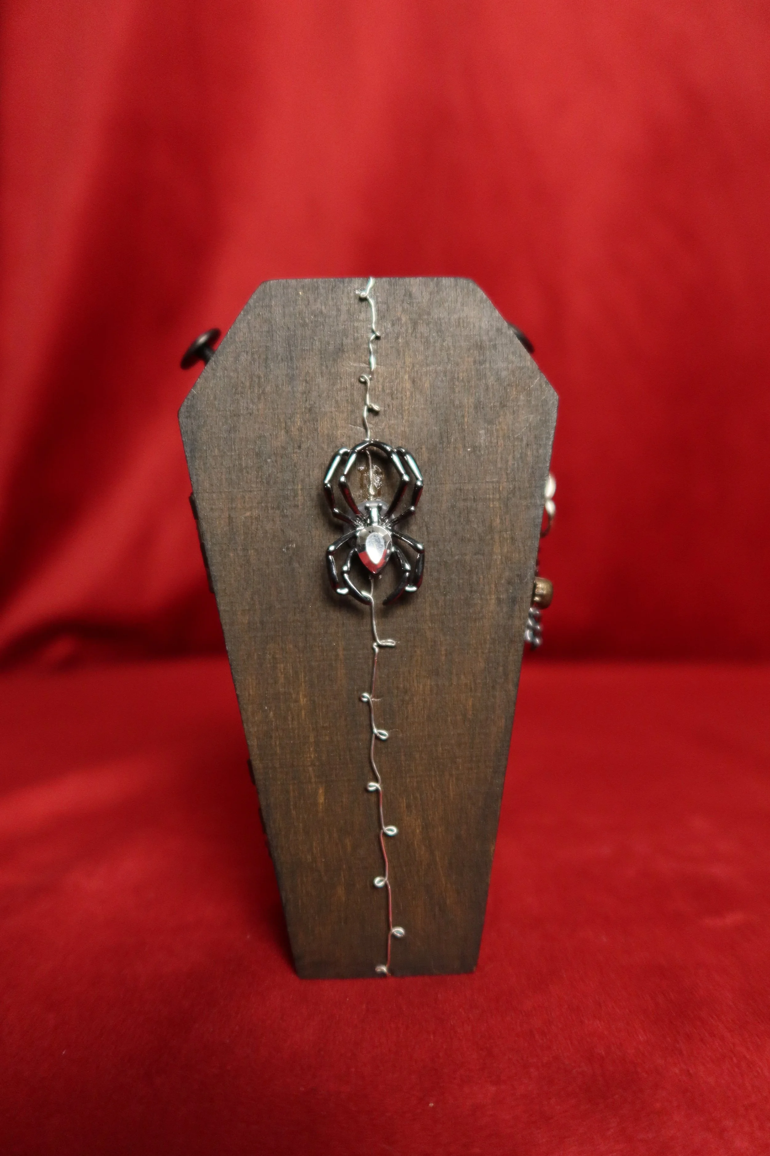 A silver spider-shaped pendant on a wire jewelry piece displayed against a red background.