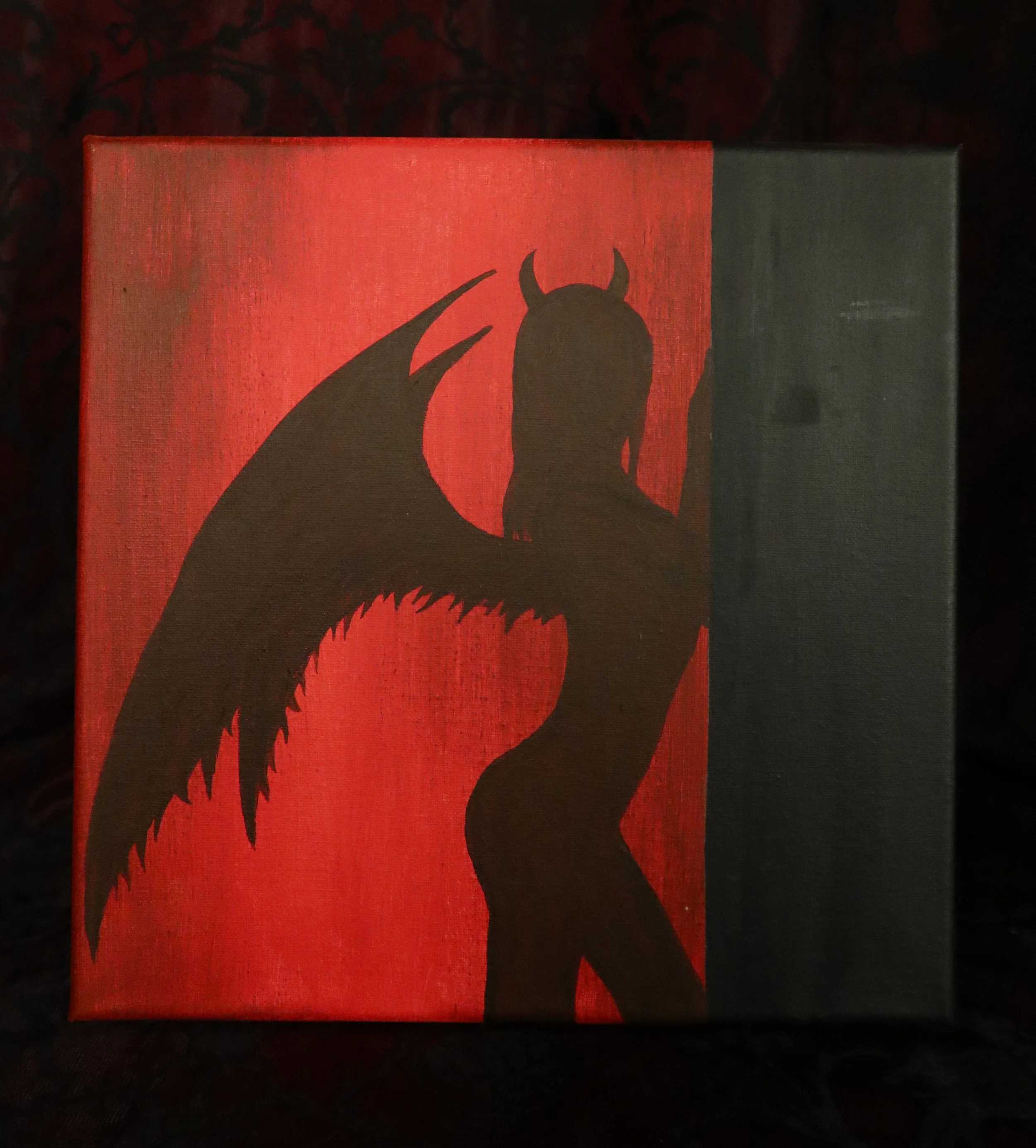 Silhouette of a devilish character with horns and clawed hands on a red and black background.