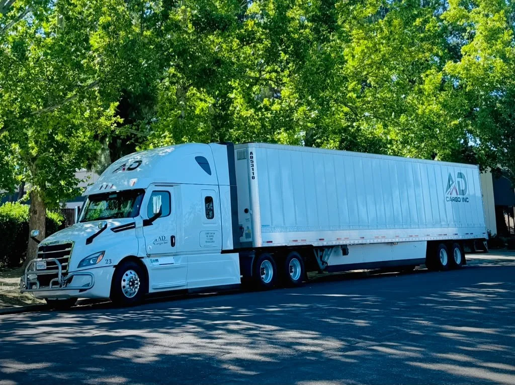 White semi-truck parked on the side of a street near green trees