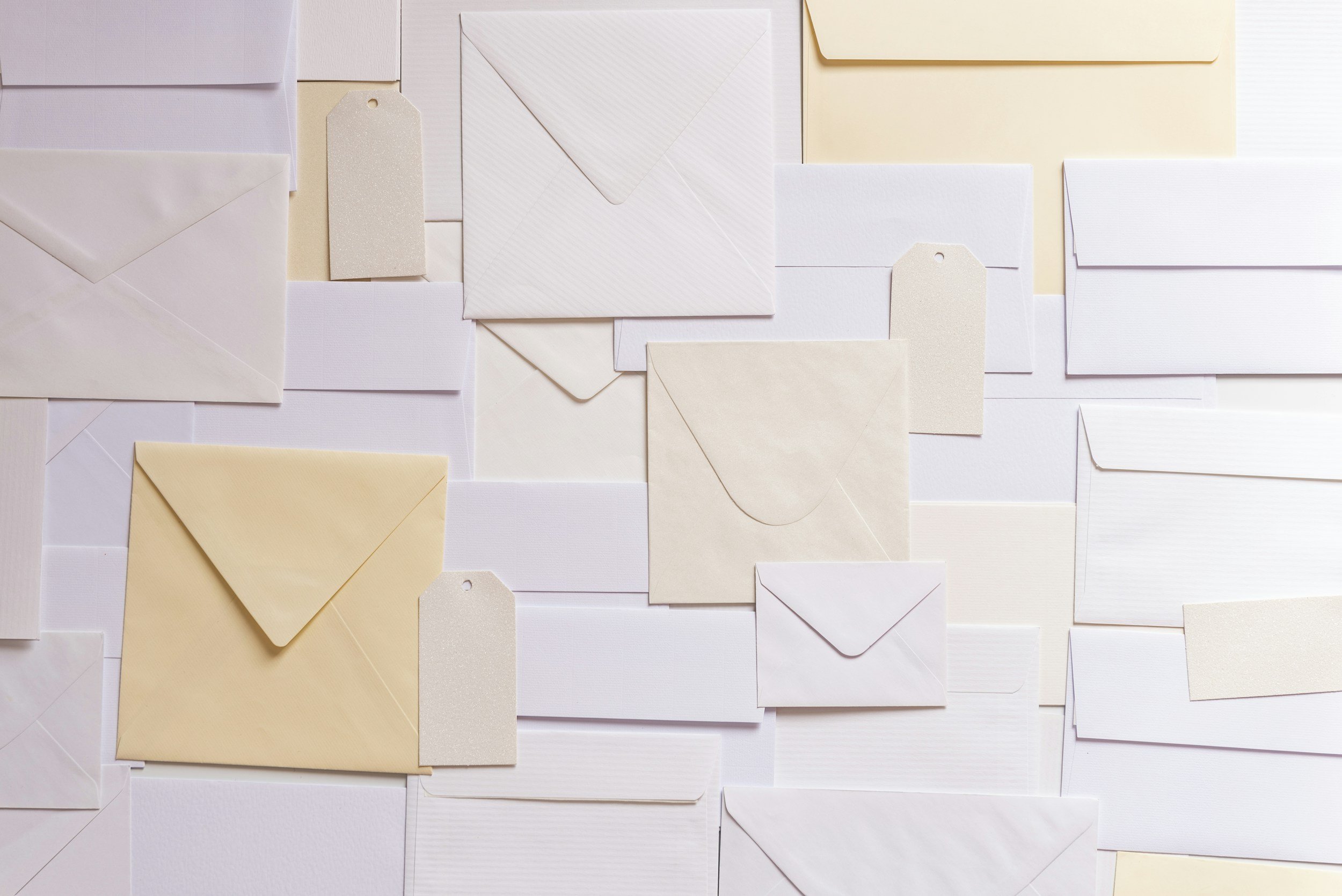 A flat lay of various white and cream envelopes arranged on a white surface, indicating a mailing list.
